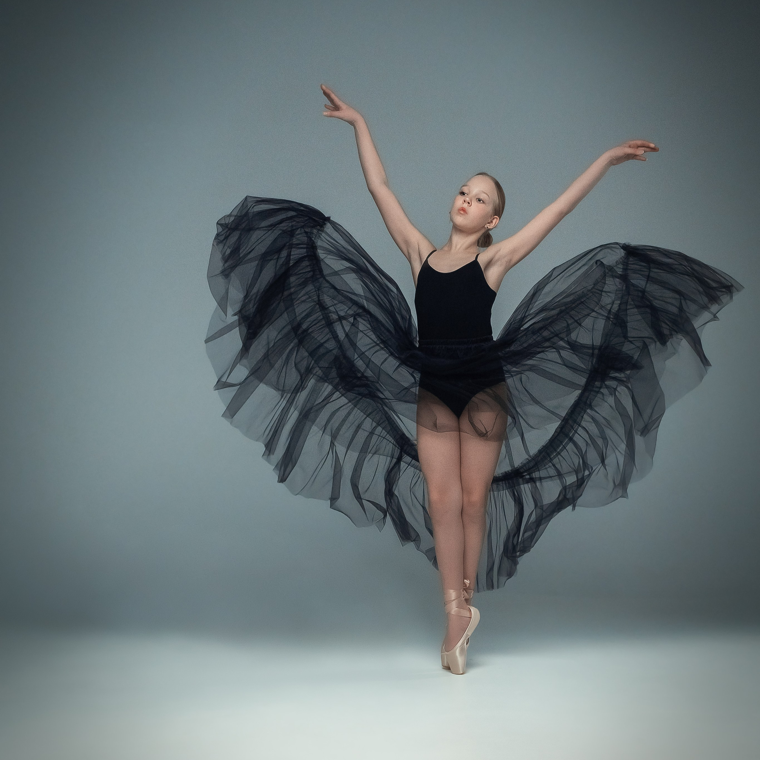 Гимнастка в элегантной позе выполняет элемент с лентой, плавно вытягивая ткань в динамичном движении, демонстрируя гибкость, грацию и выразительность художественной гимнастики