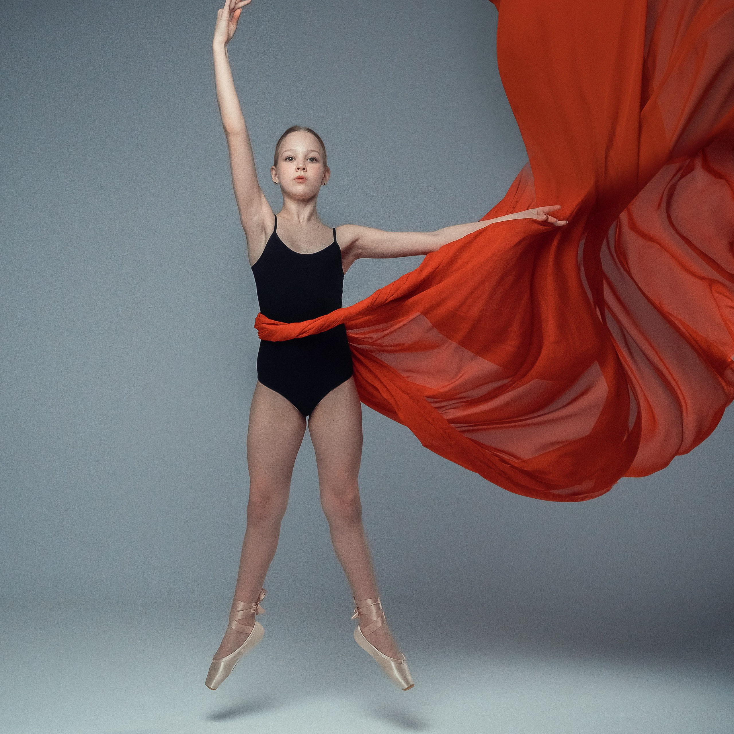 Гимнастка в элегантной позе выполняет элемент с лентой, плавно вытягивая ткань в динамичном движении, демонстрируя гибкость, грацию и выразительность художественной гимнастики