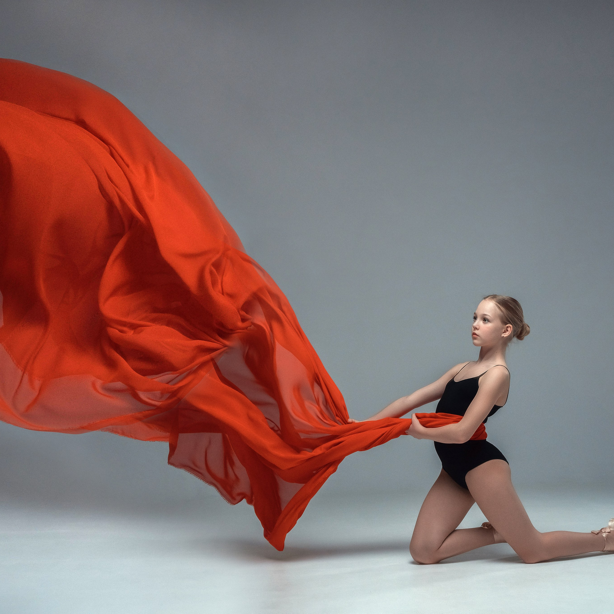 Гимнастка в элегантной позе выполняет элемент с лентой, плавно вытягивая ткань в динамичном движении, демонстрируя гибкость, грацию и выразительность художественной гимнастики