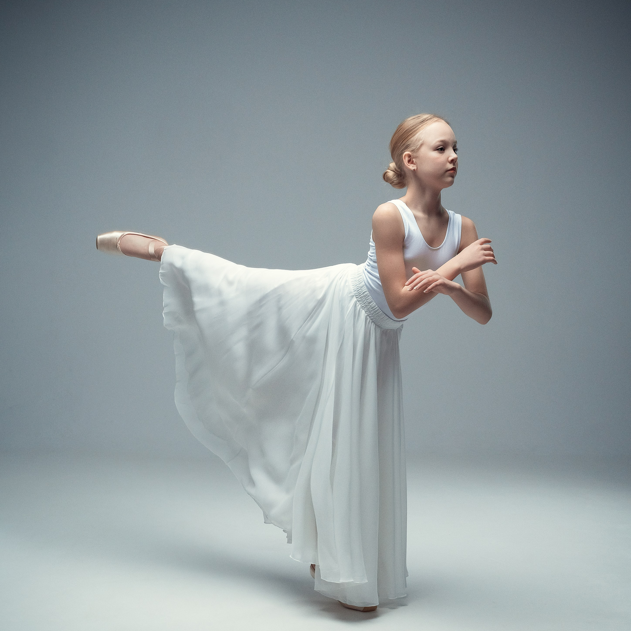 Гимнастка в элегантной позе выполняет элемент с лентой, плавно вытягивая ткань в динамичном движении, демонстрируя гибкость, грацию и выразительность художественной гимнастики