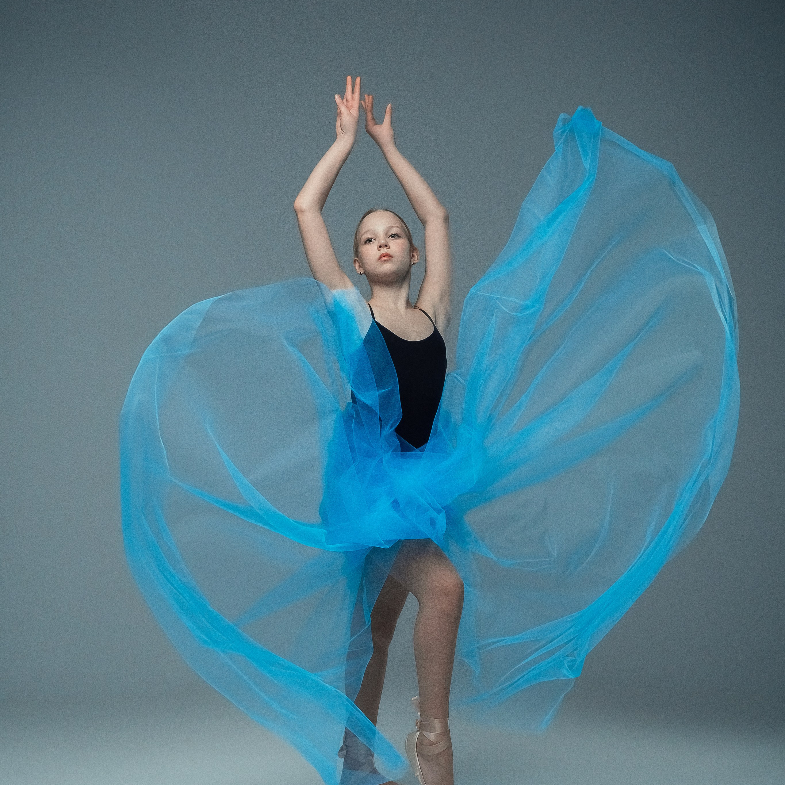 Гимнастка в элегантной позе выполняет элемент с лентой, плавно вытягивая ткань в динамичном движении, демонстрируя гибкость, грацию и выразительность художественной гимнастики