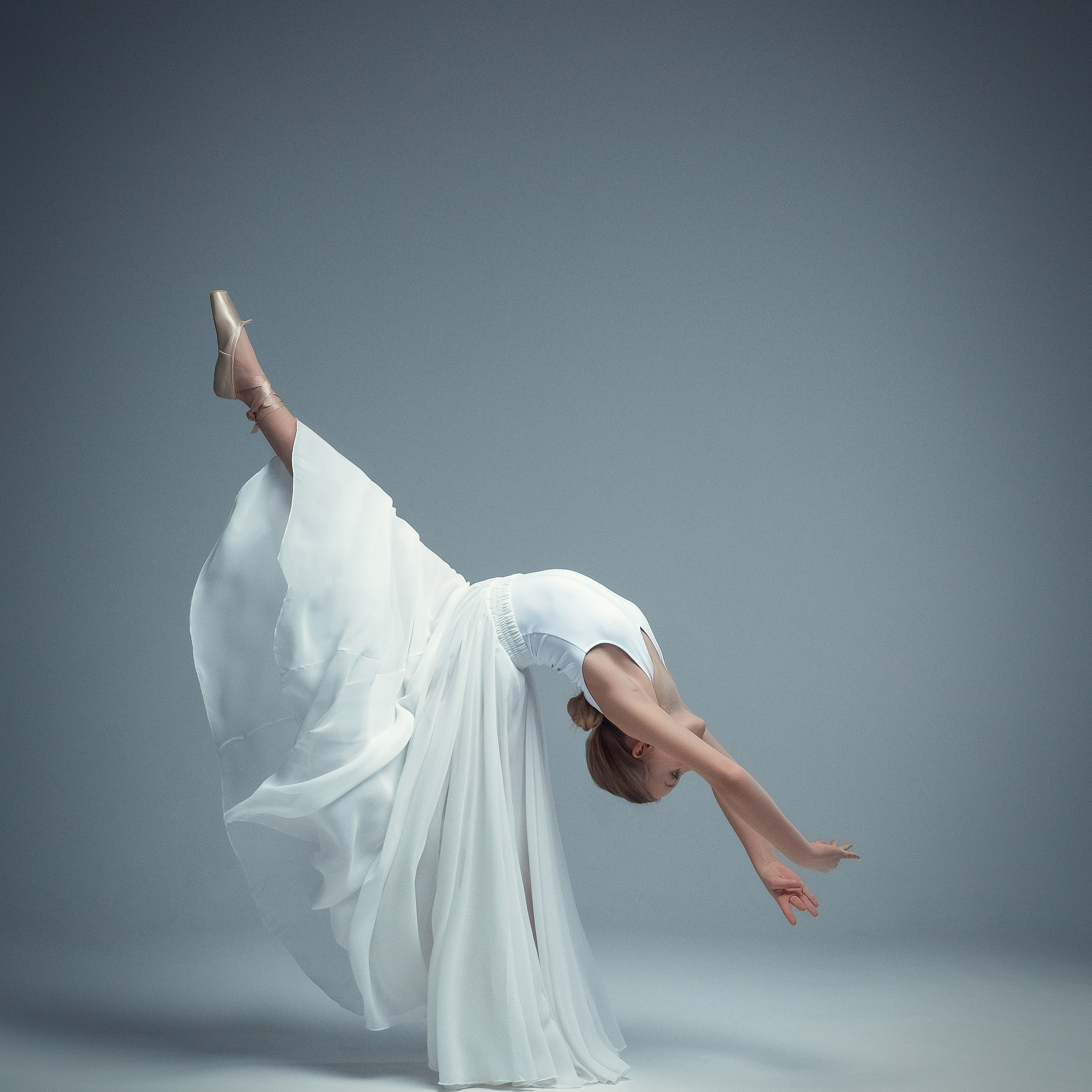 Гимнастка в элегантной позе выполняет элемент с лентой, плавно вытягивая ткань в динамичном движении, демонстрируя гибкость, грацию и выразительность художественной гимнастики