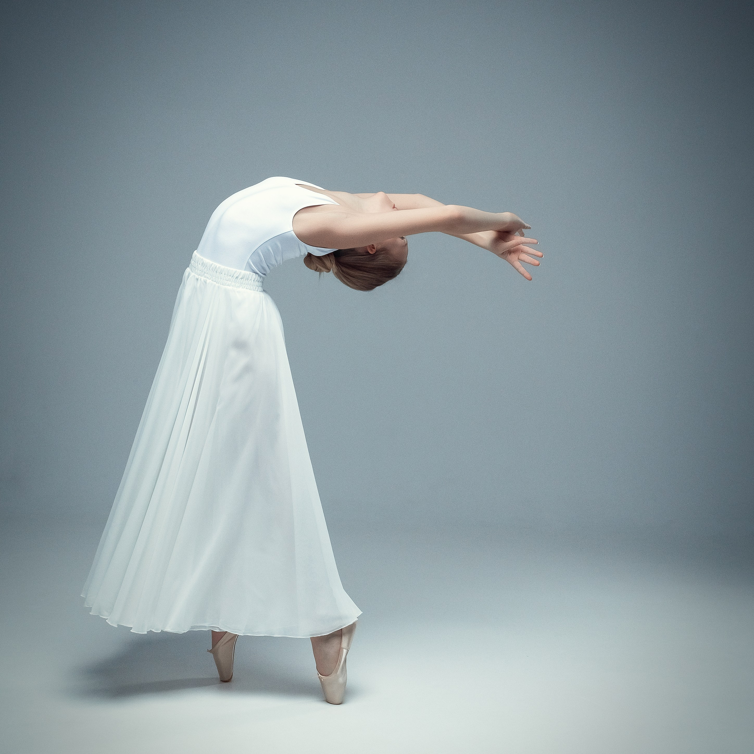 Гимнастка в элегантной позе выполняет элемент с лентой, плавно вытягивая ткань в динамичном движении, демонстрируя гибкость, грацию и выразительность художественной гимнастики