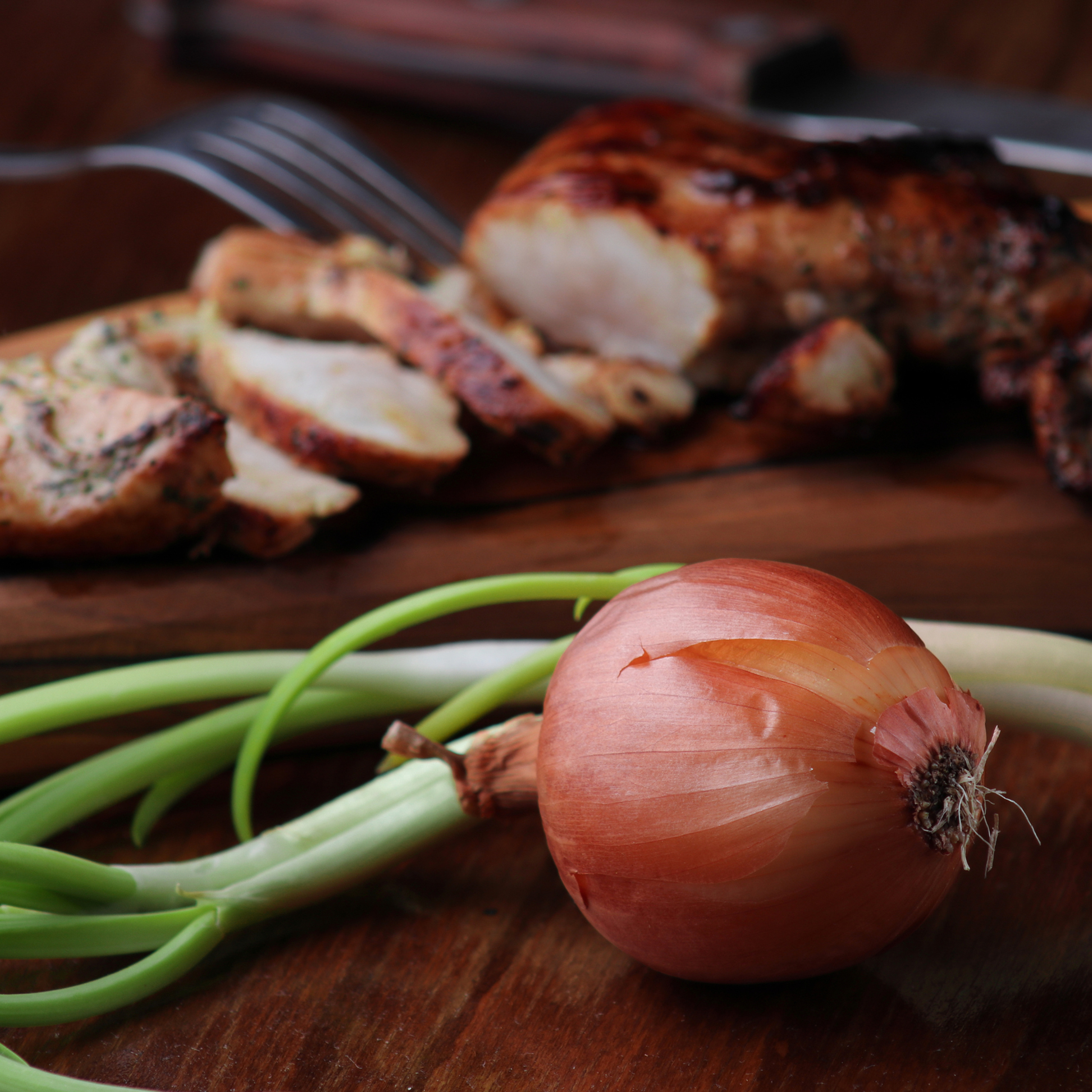 Жареное мясо на разделочной доске и зеленый лук.