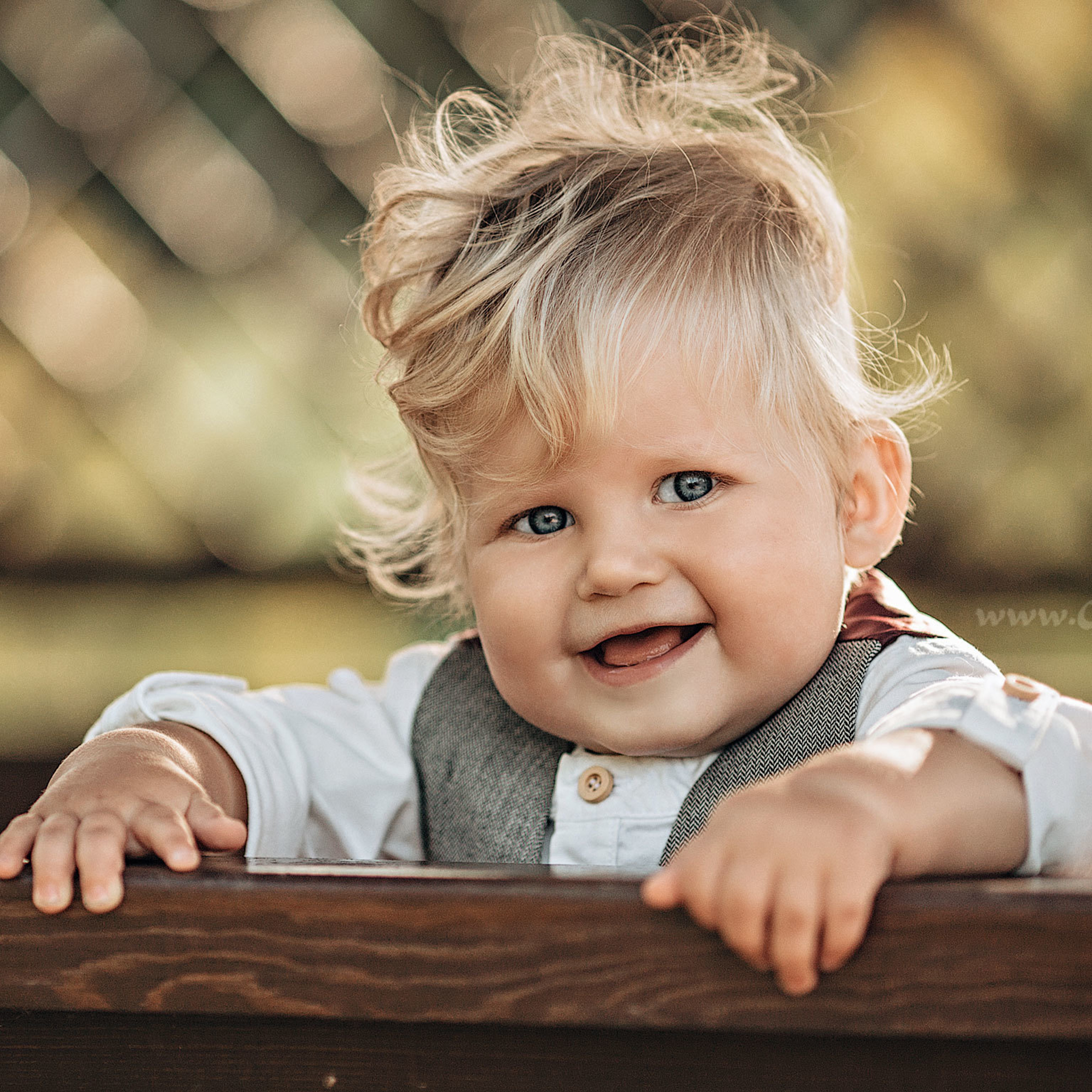 Милый малыш с кудрявами светлыми волосами 1 года улыбается