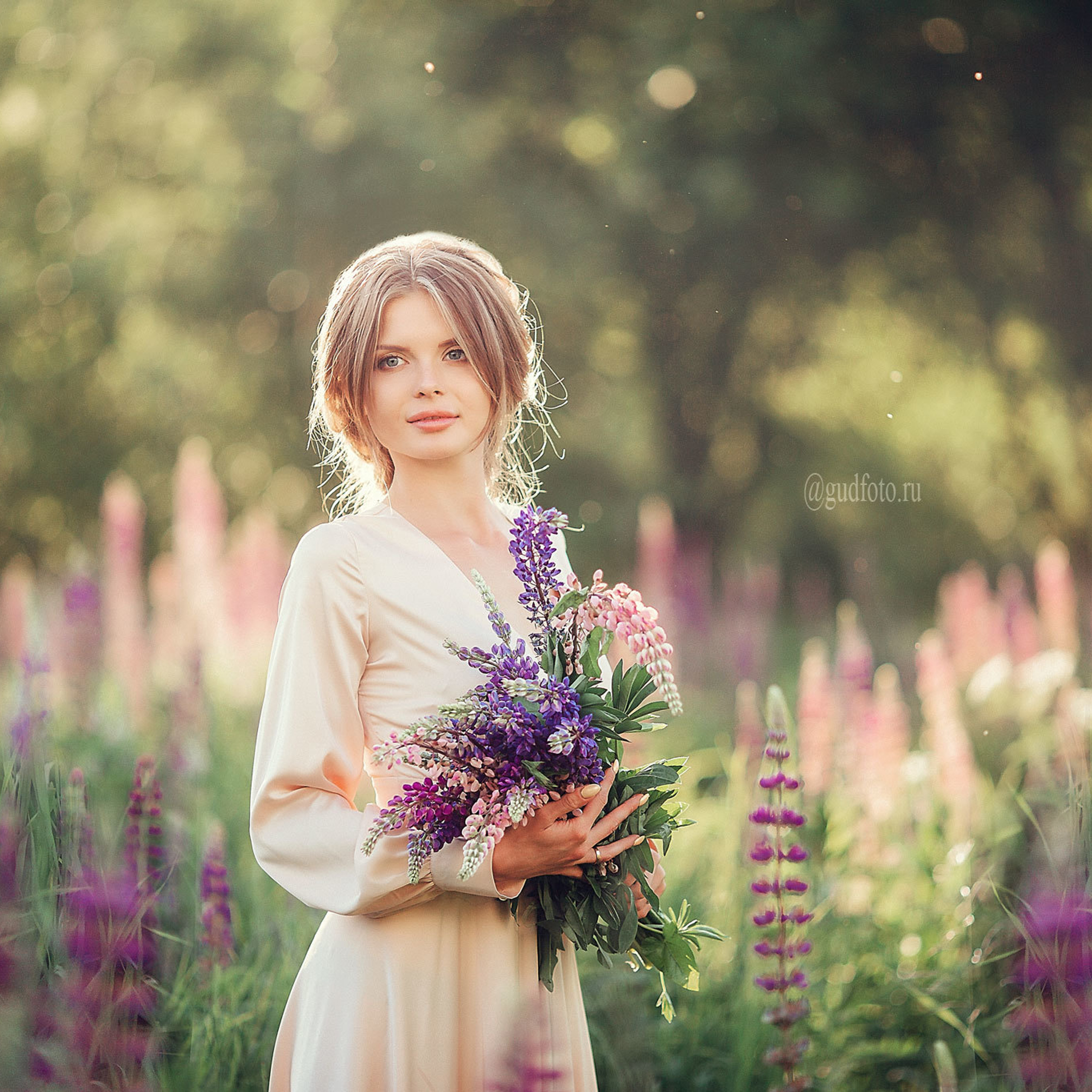 Девушка в светлом розовом бежевом платье в поле с цветами  люпинов летом и весной