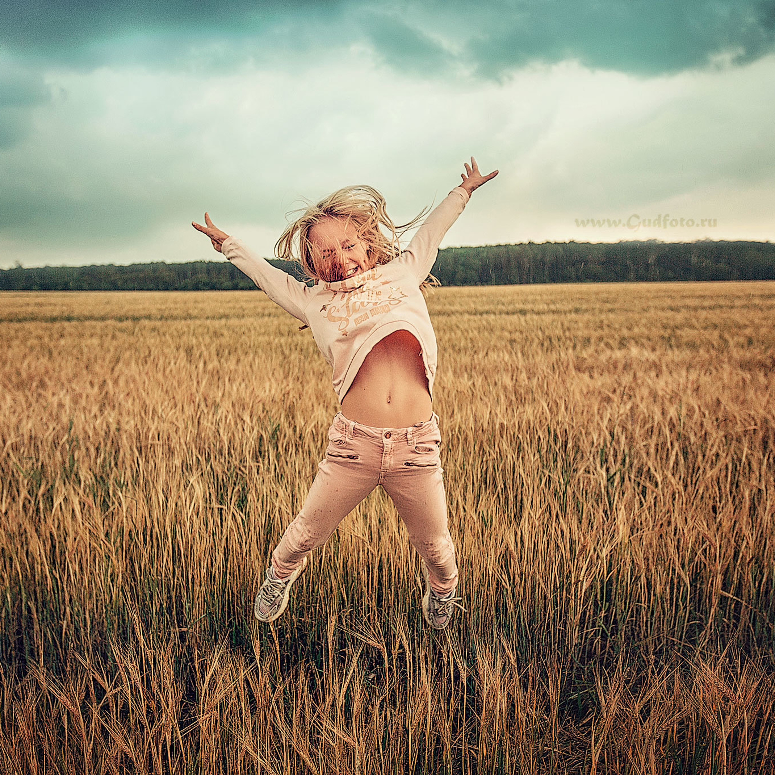 Радостная девочка прыгает по пшеничному полю на закате после дождя
