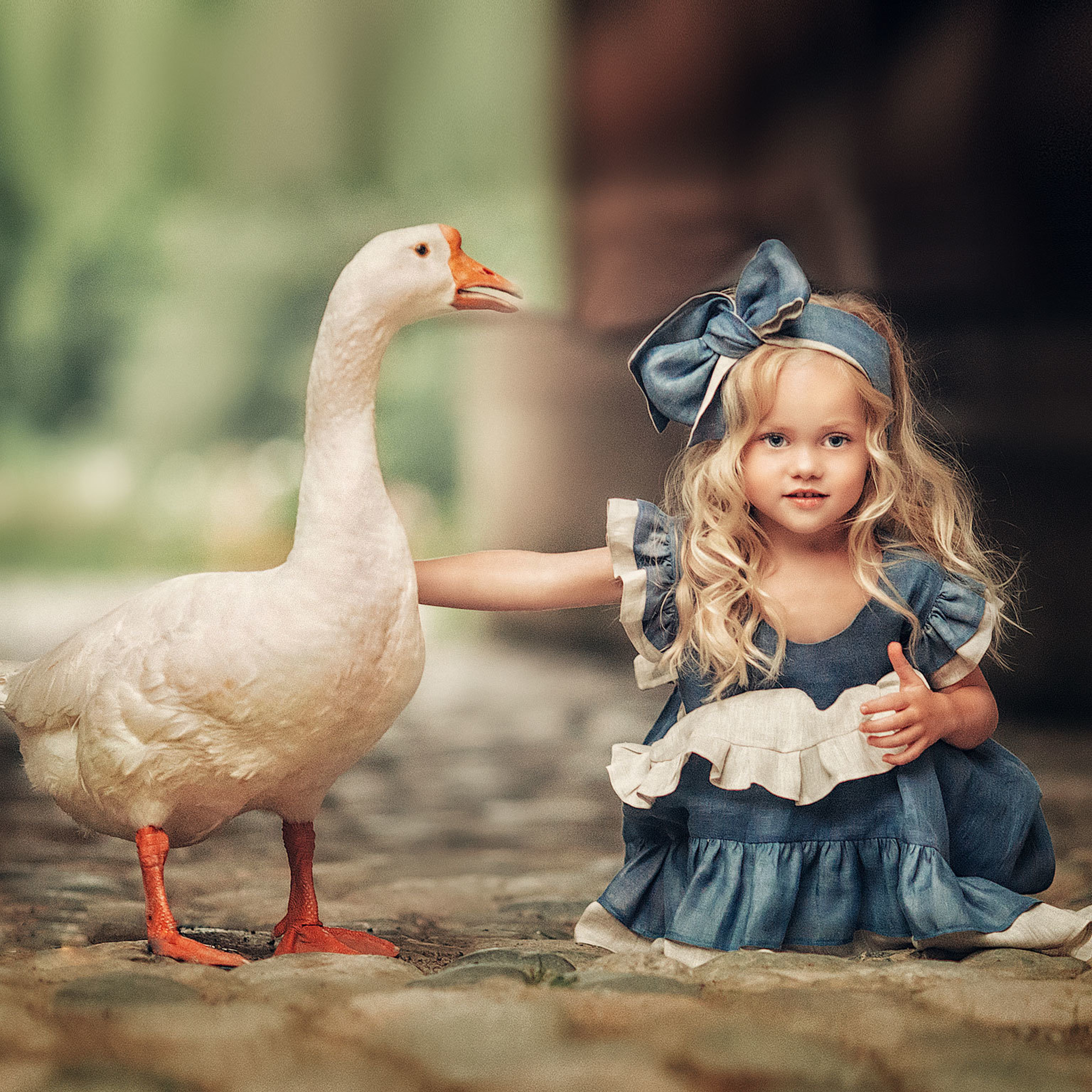 Красивая девочка Виола блондинка сидит на камнях с белым гусем в парке Коломенское