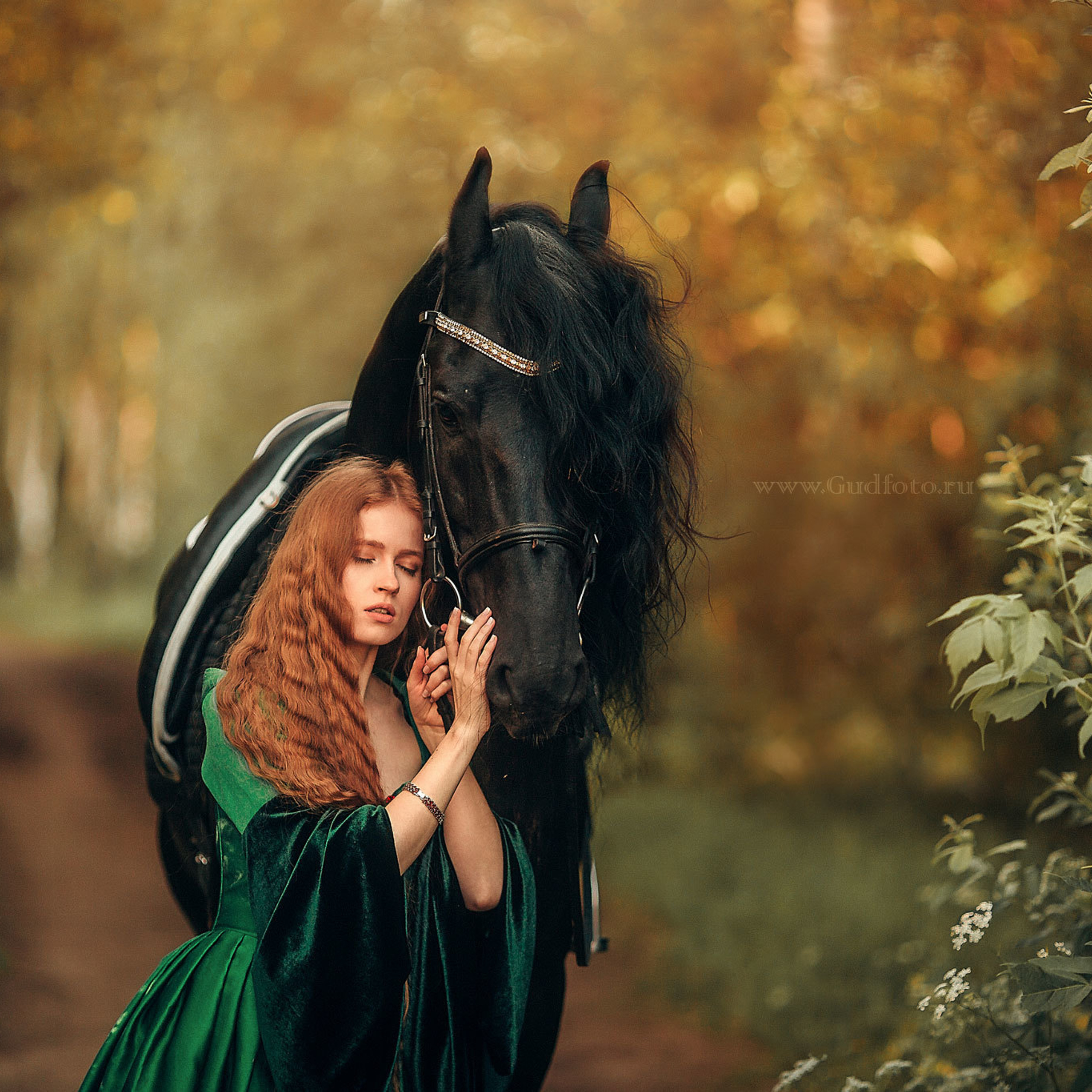 Рыжая русская  девушка с длинными волосами с черным конем летом в зеленом платье в  траве в лесу в парке