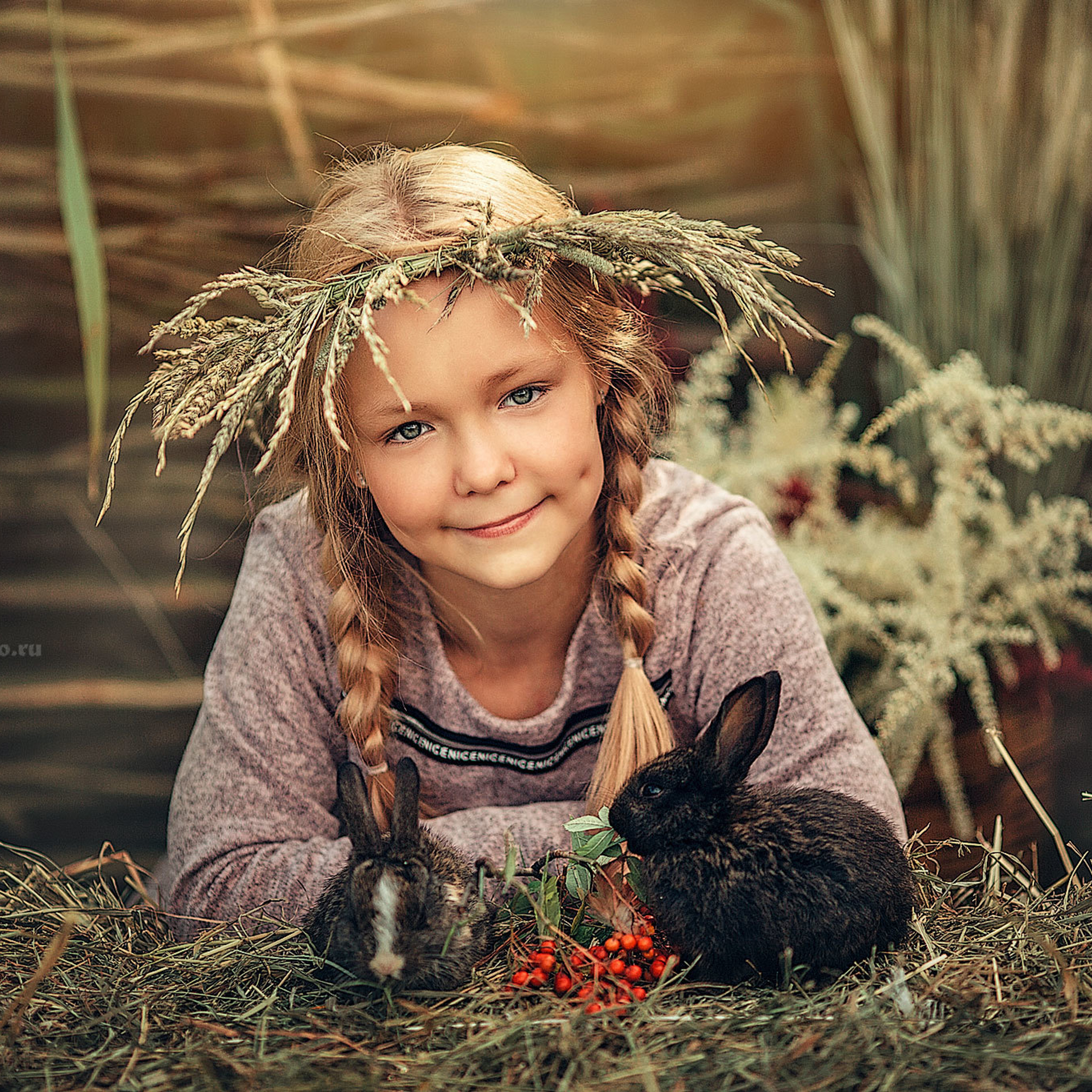 Девочка в венке из цветов на голове лежит на сене рядом с кроликами