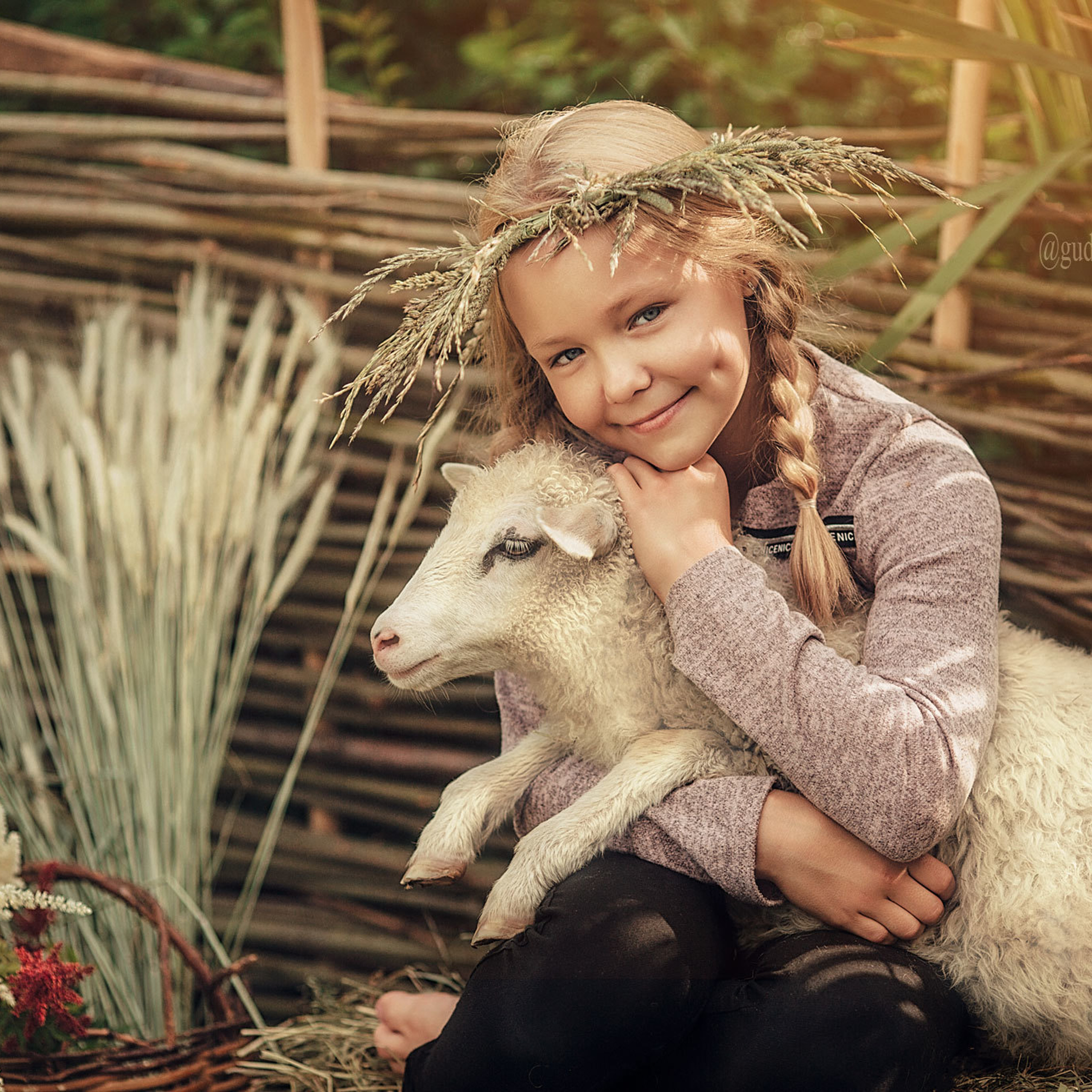 Девочка в венке из цветов на голове держит в руках барашка