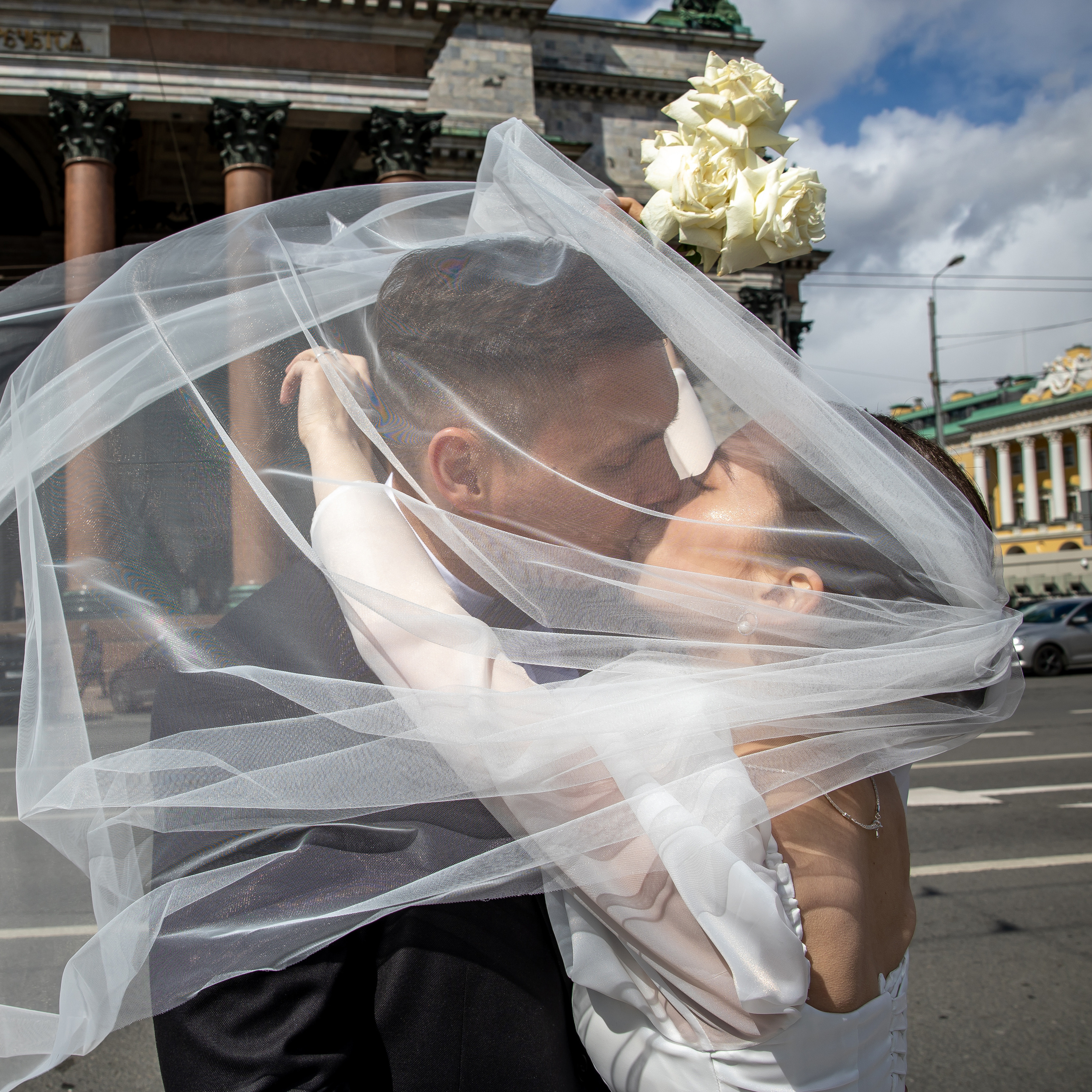 Фотограф интересно снимает свадебную прогулку. Невеста целует жениха.