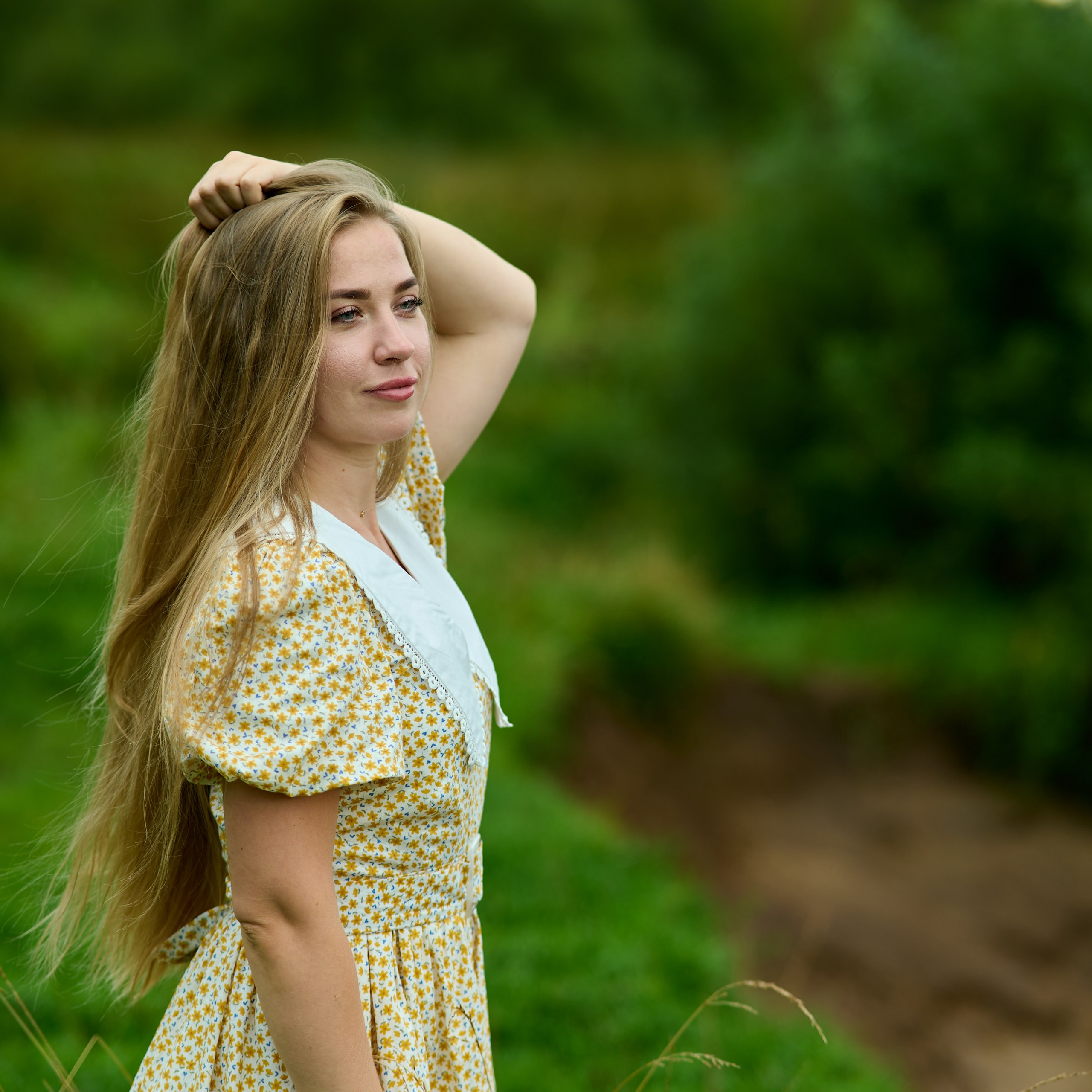 Крупный план портрета, рука у волос рядом с серьгой, размытый зелёный фон
