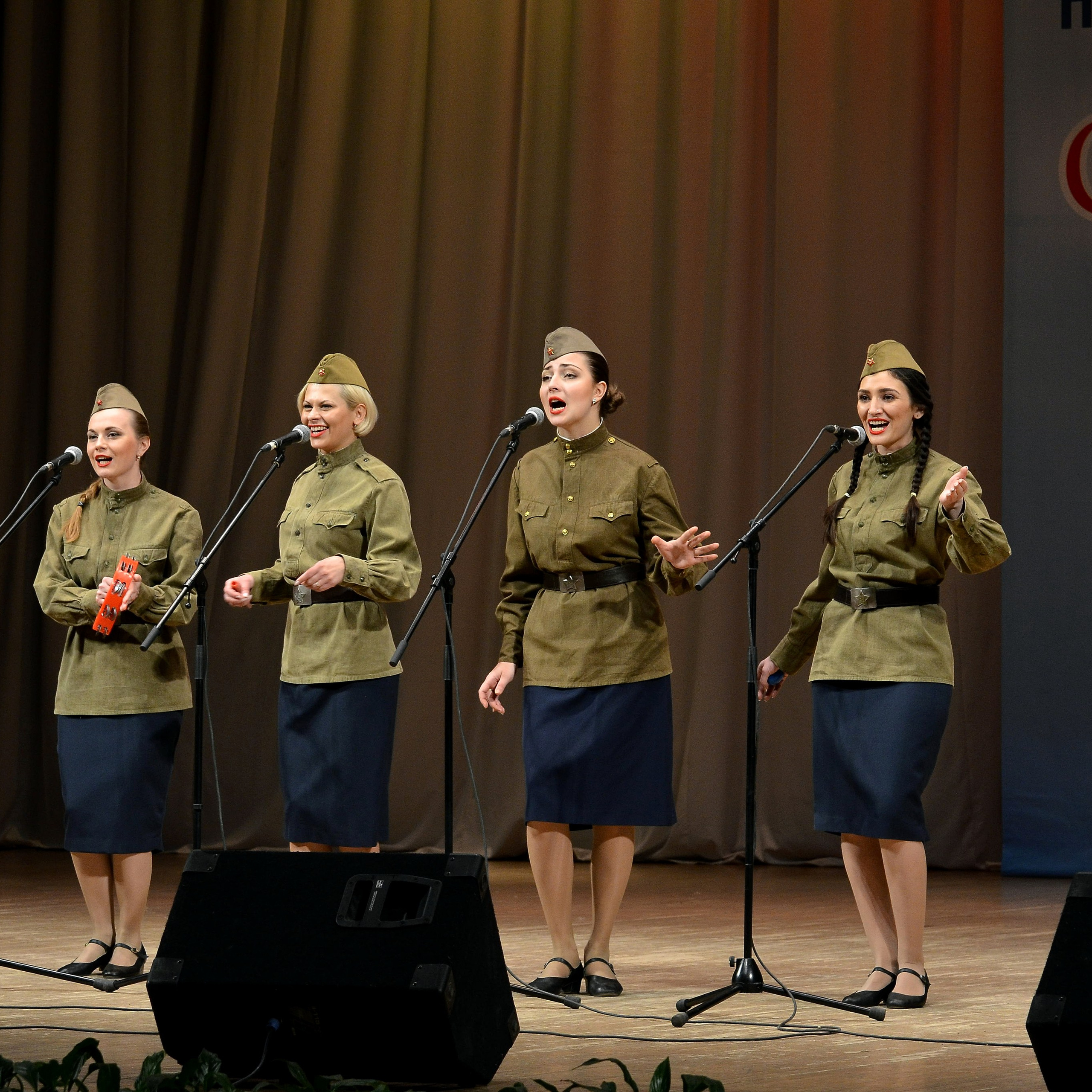 Ансамбль в светлых костюмах на тёмной сцене, полукруг