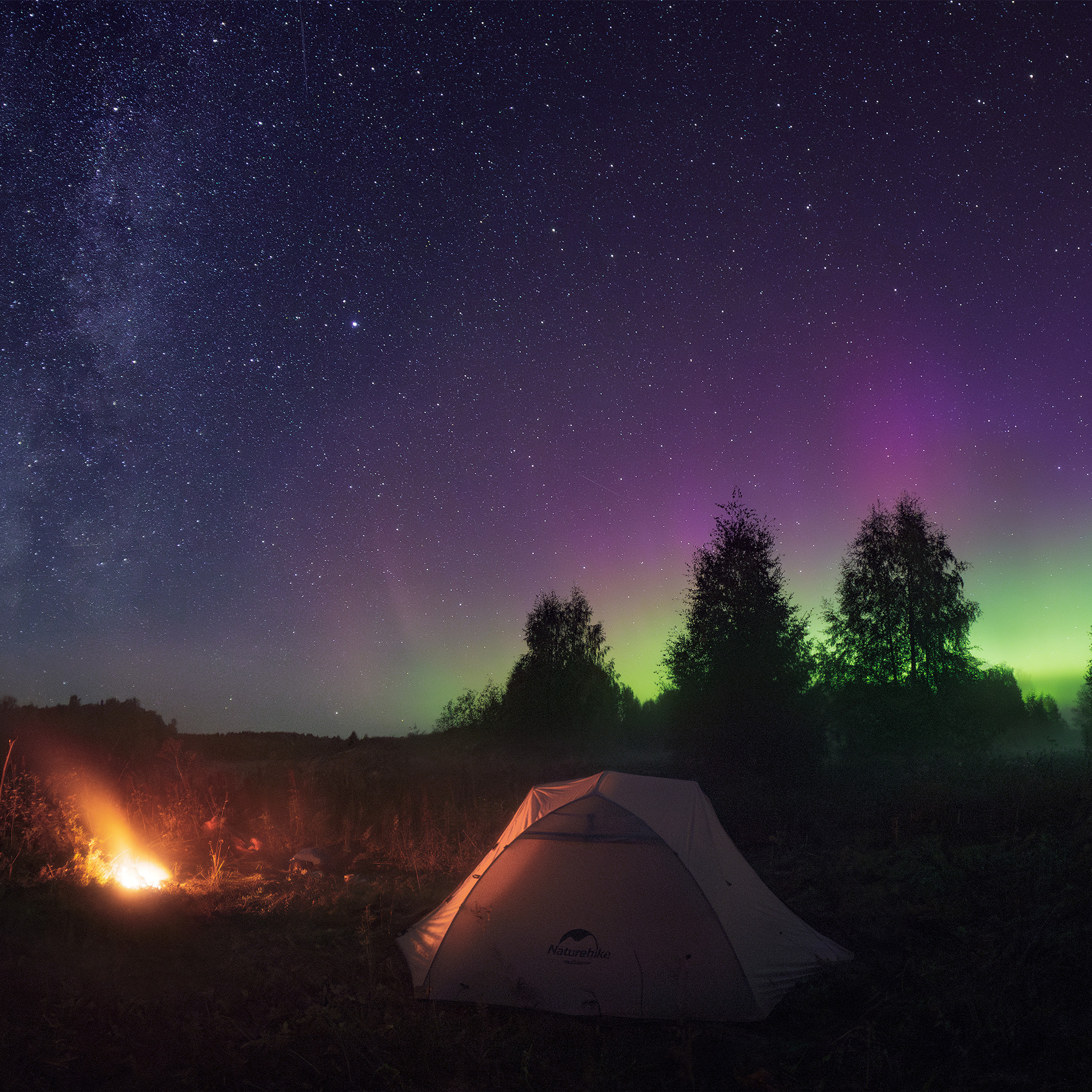 Aurora borealis. Northern lights on the shores of Vychegda in the Komi Republic. Panorama of the Northern Lights and the Milky Way. Night landscape with Northern Lights. Tent and fire against the background of the Milky Way and Northern Lights.