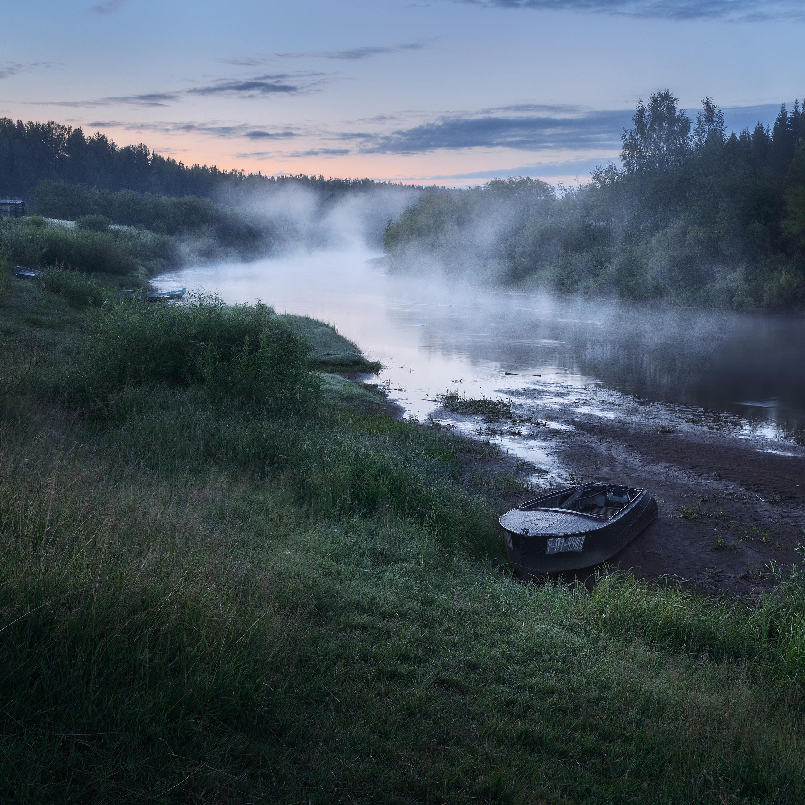 White nights in the north. Fog on the river. Boats on the banks of the river Voch.