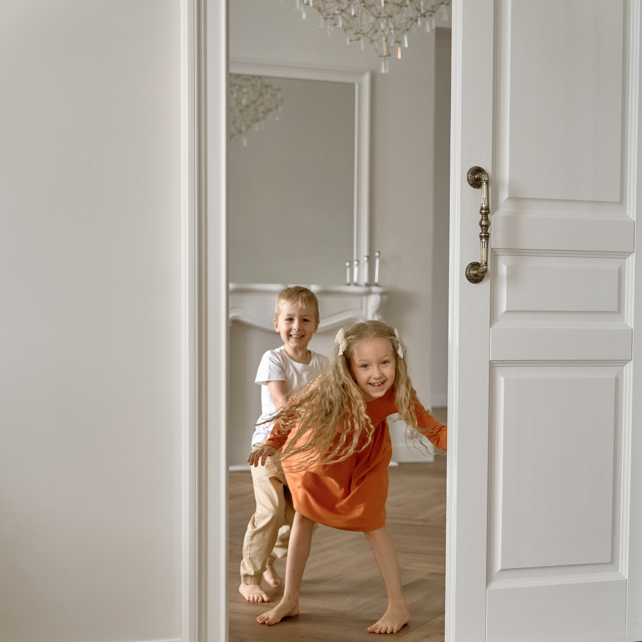Семейная фотосессия дети бегут из комнаты через открытую дверь, за ними видна люстра и камин