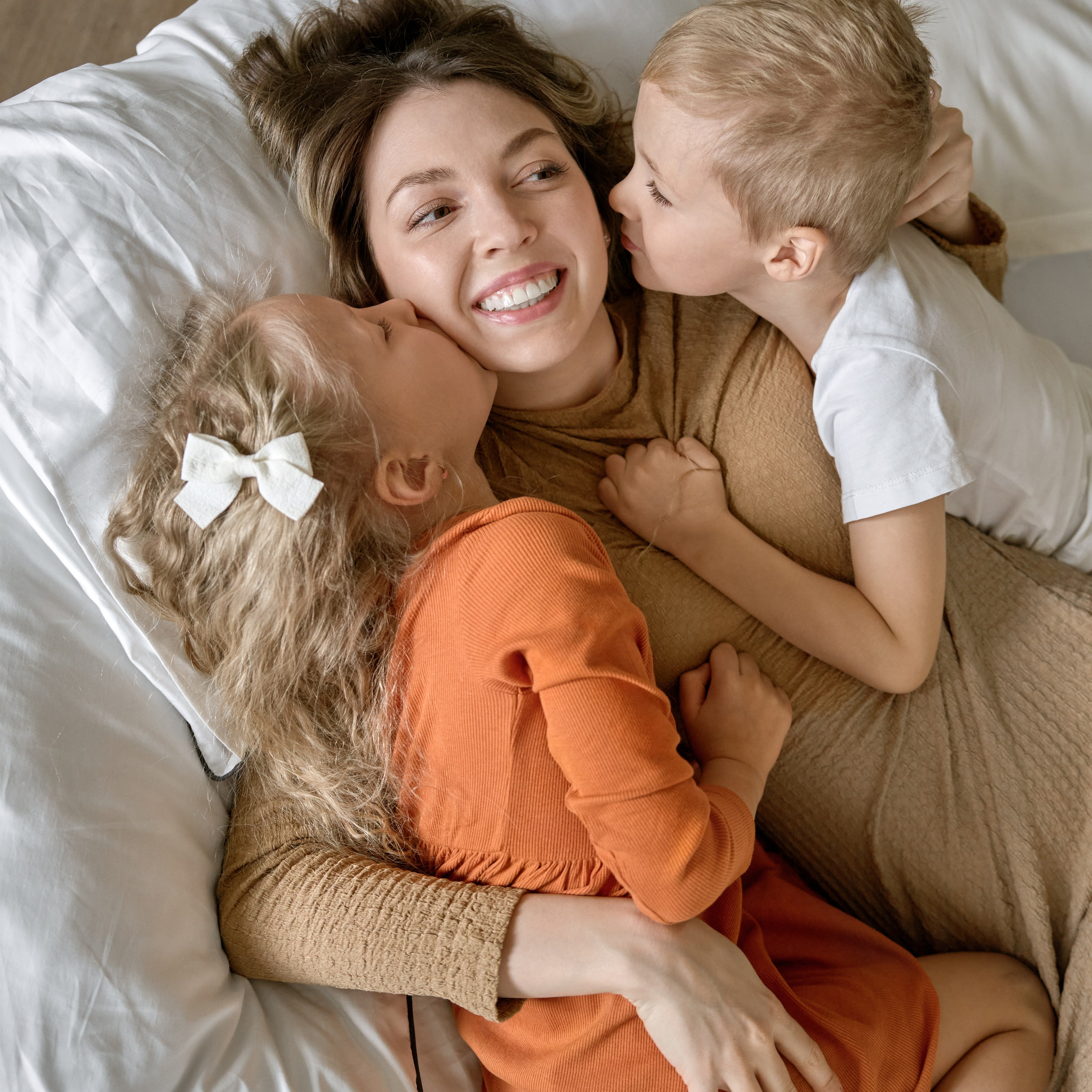 Идеальная семейная фотография: мама и дети обнимаются на кровати. Момент любви и счастья, снятый сверху