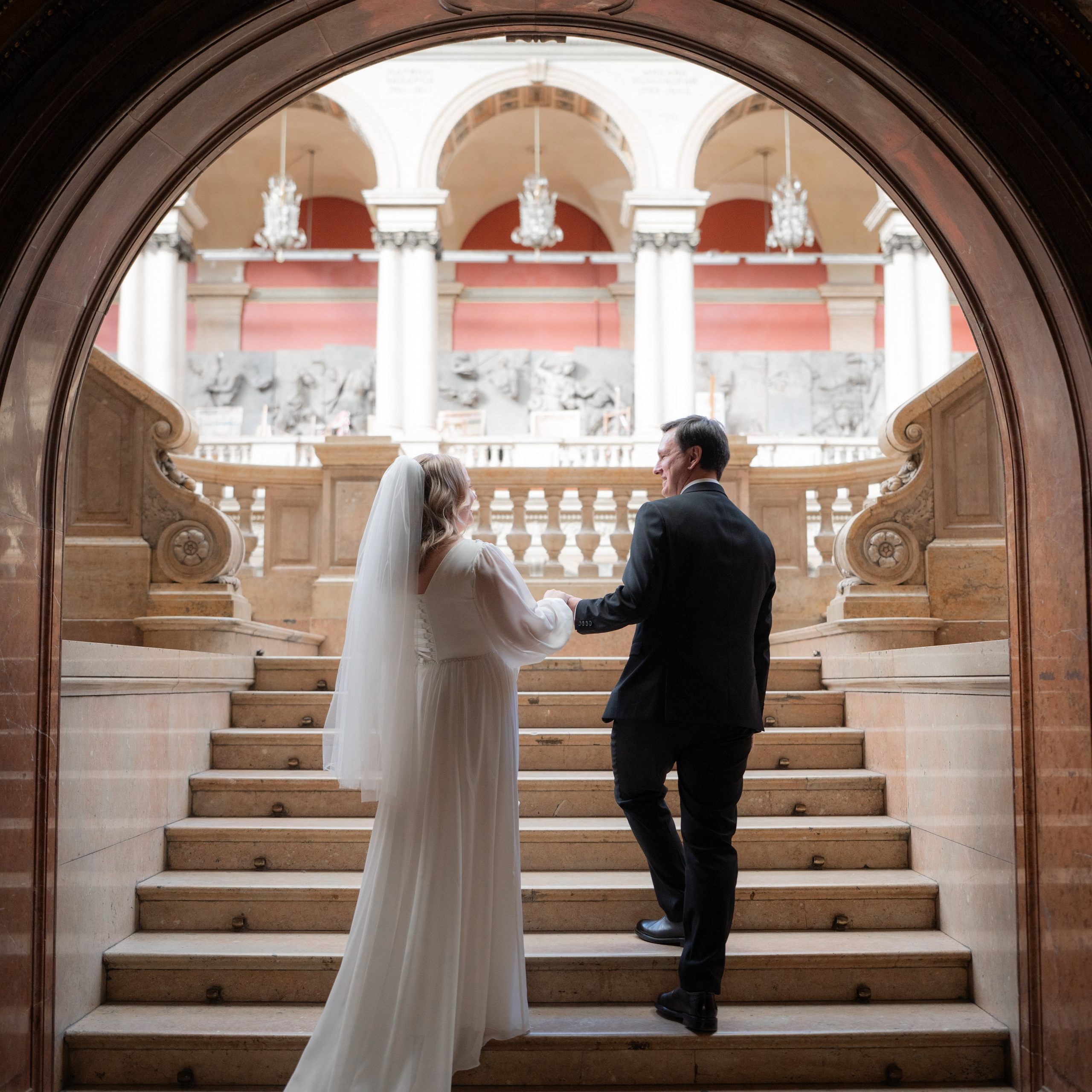 Свадебная фотосессия в академии Штиглица в Санкт-Петербурге невеста и жених идут за руки лестнице входя в арку.