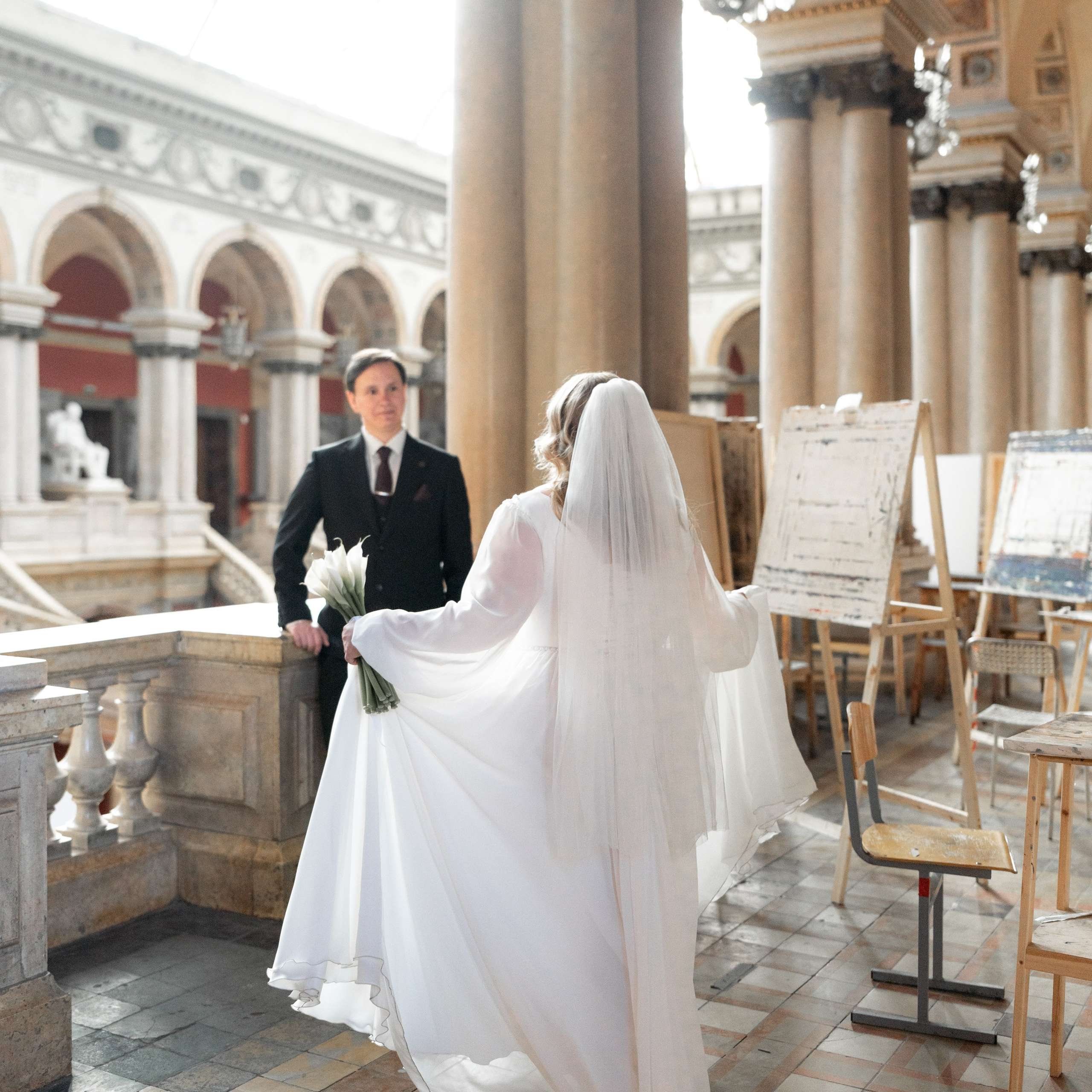 Свадебная фотосессия в академии Штиглица в Санкт-Петербурге невеста подходит к жениху в лучах солнечного света.