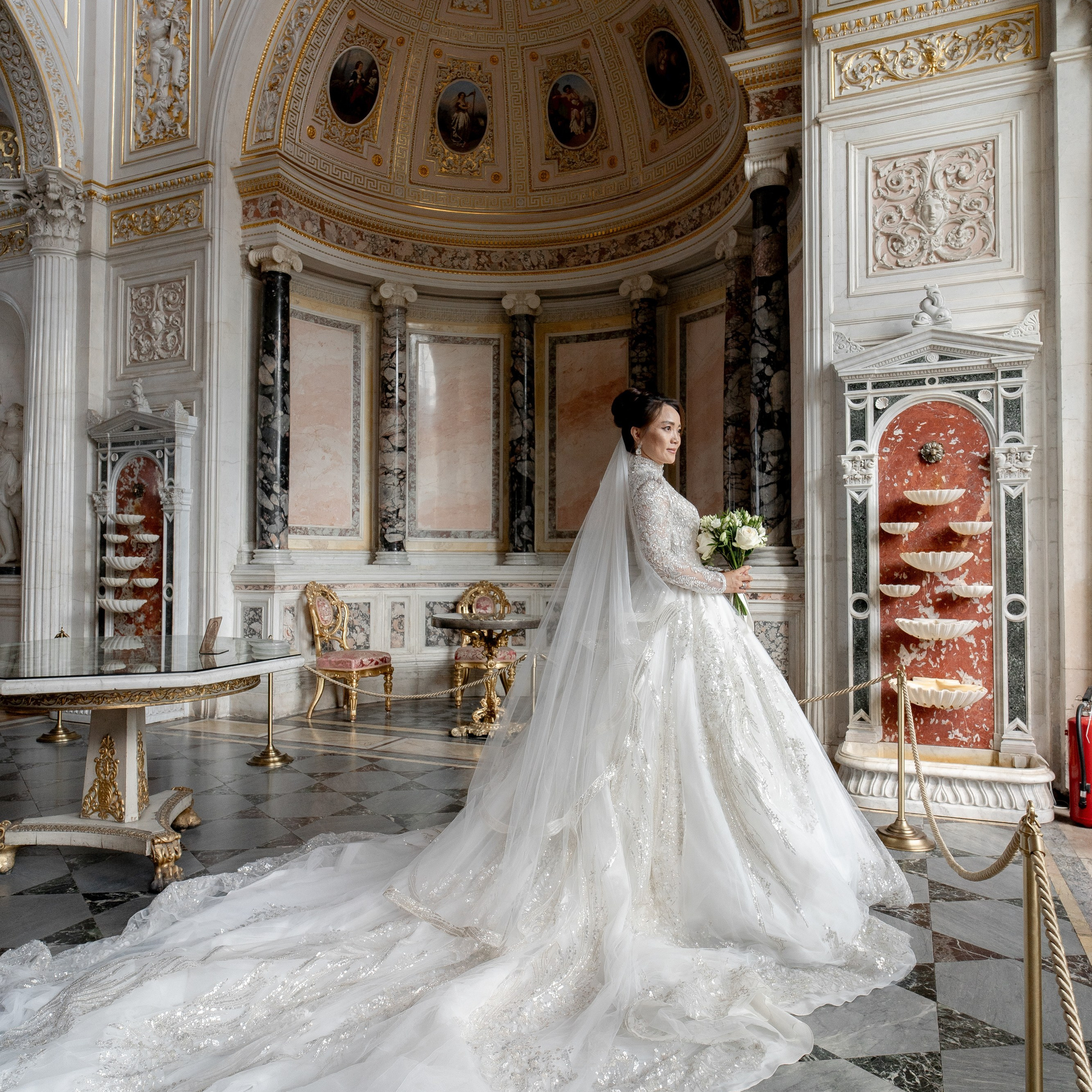 Свадебная фотосессия в Эрмитаже невеста в платье с большим шлейфом стоит у окна