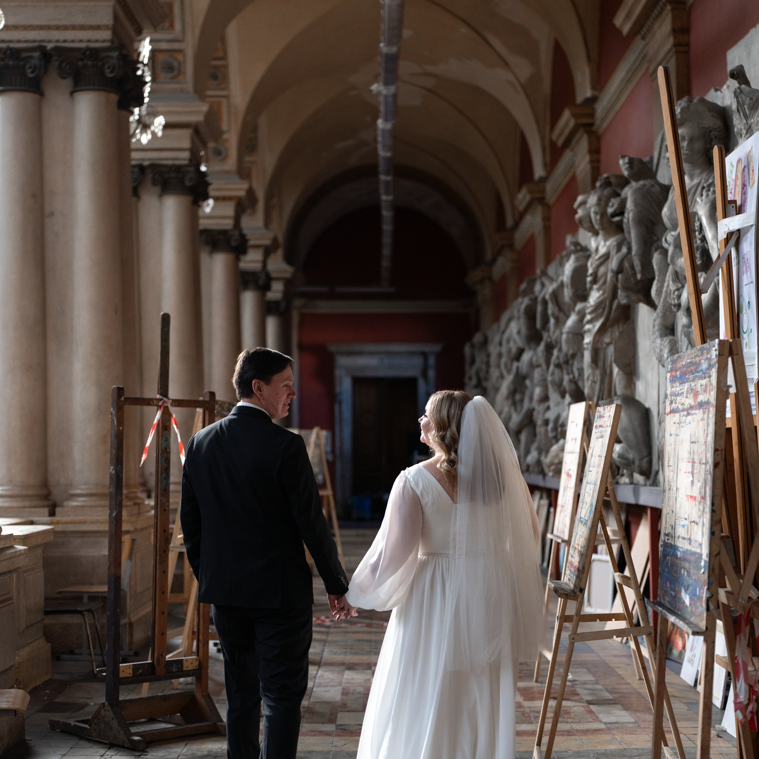 Свадебная фотосессия в академии Штиглица в Санкт-Петербурге невеста и жених идут за руки по коридору.