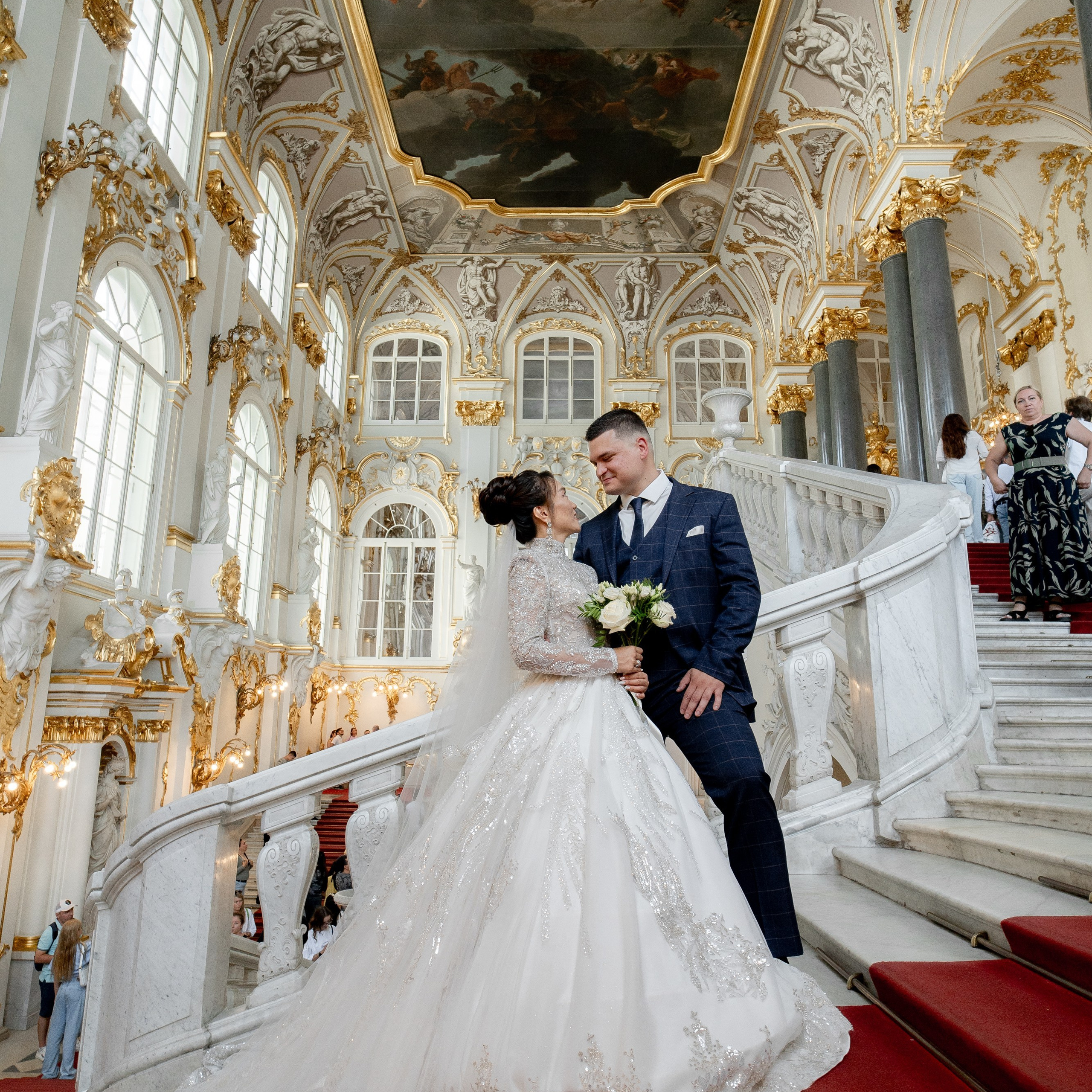 Свадебная фотосессия в Эрмитаже жених и невеста в платье с большим шлейфом стоят на главной лестнице