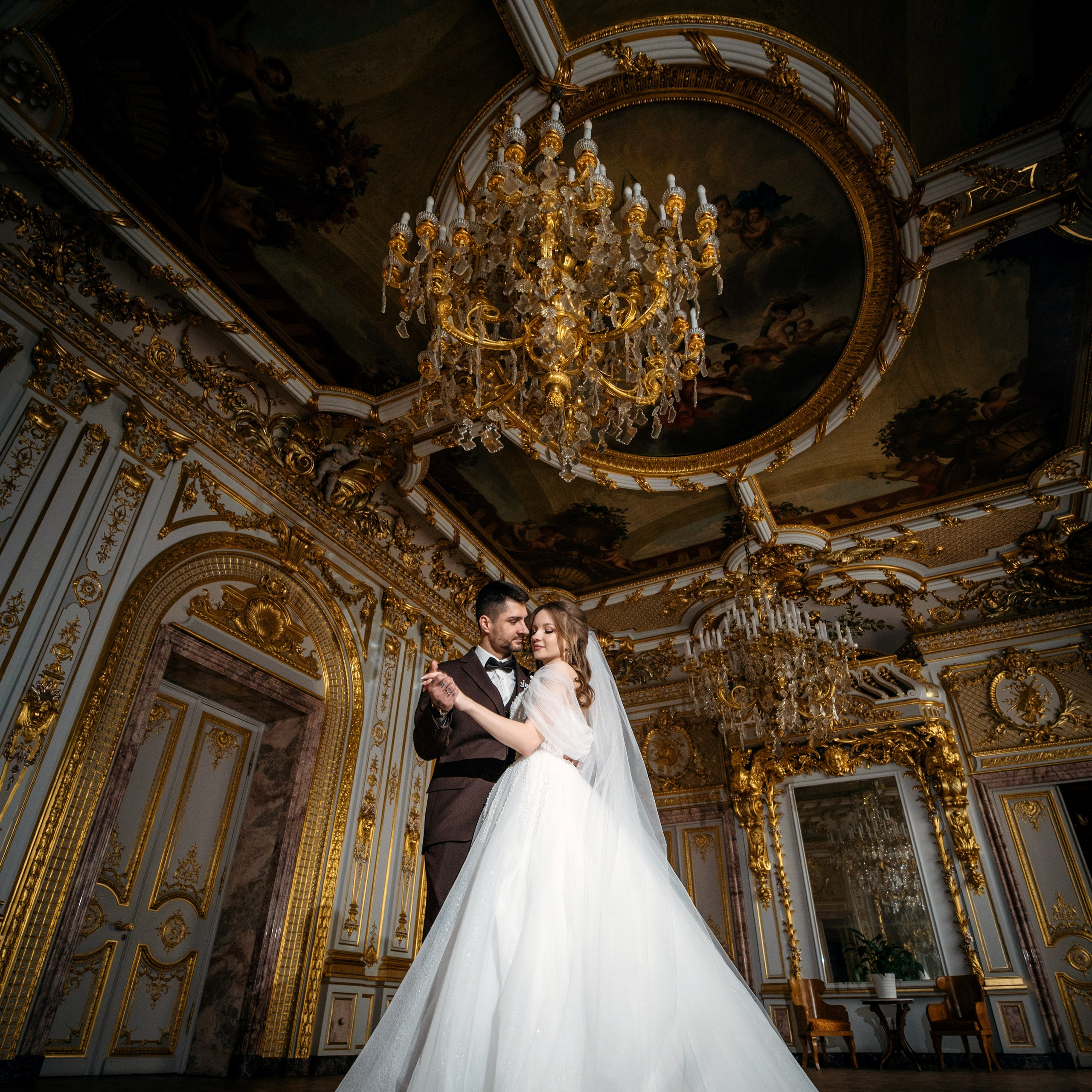 Свадебная фотосессия в особняке Половцева (дом Архитектора) невеста и жених танцуют в большом зале с золотыми люстрами и хорошо виден потолок