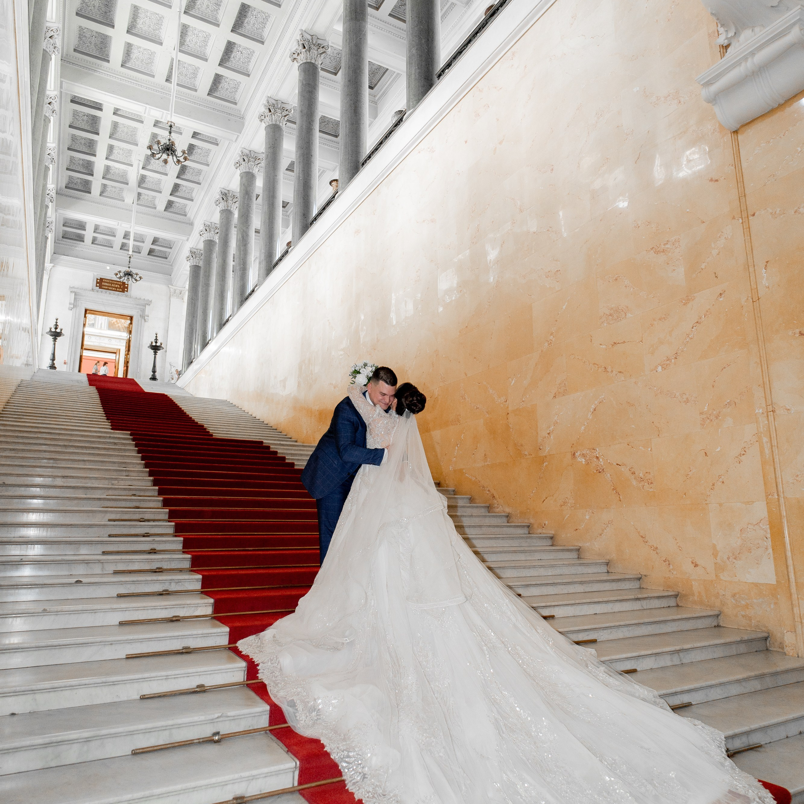 Свадебная фотосессия в Эрмитаже жених и невеста в платье с большим шлейфом целуются на лестнице