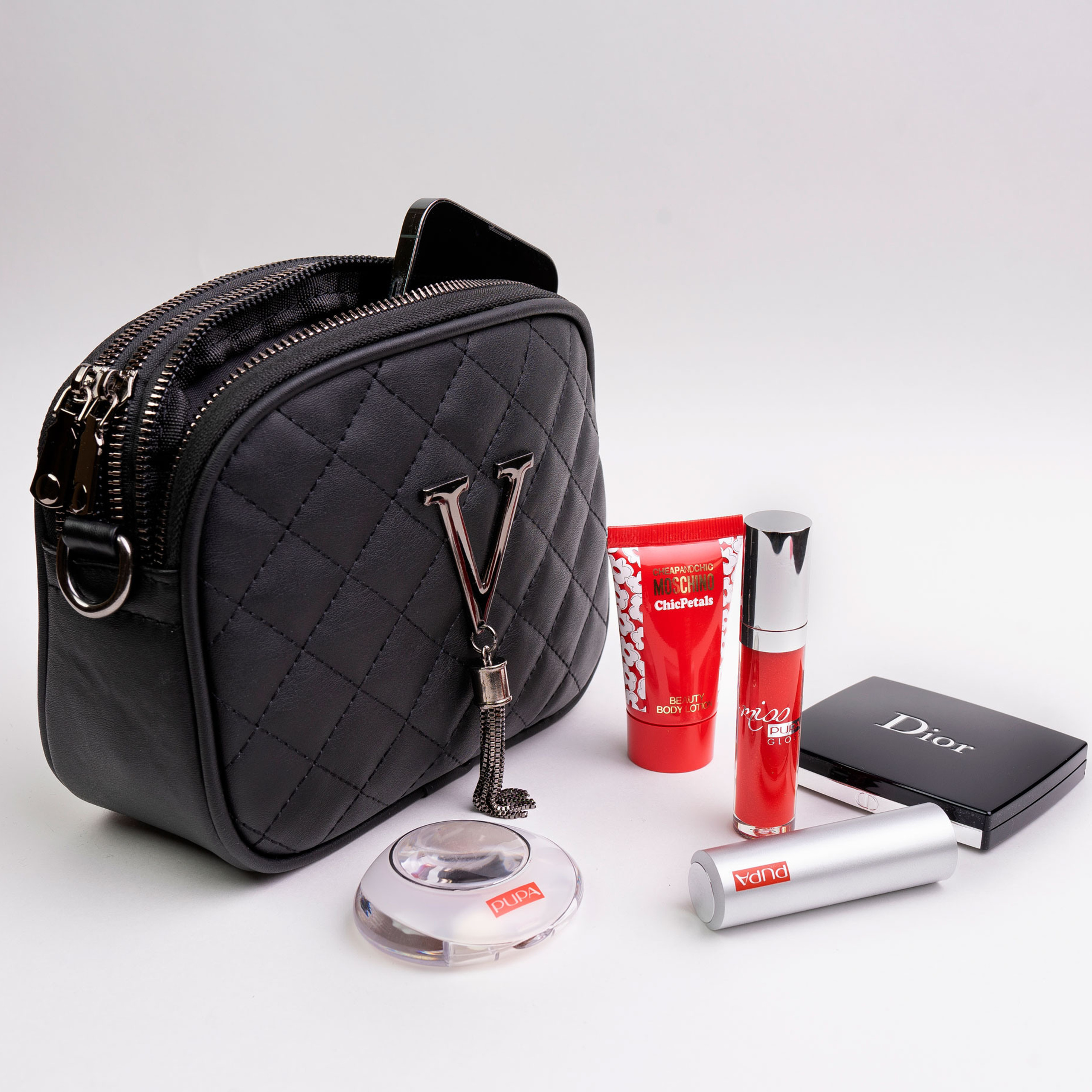 Чёрная кожаная сумка с вынутой из неё косметикой и торчащим смартфоном на белом фоне 