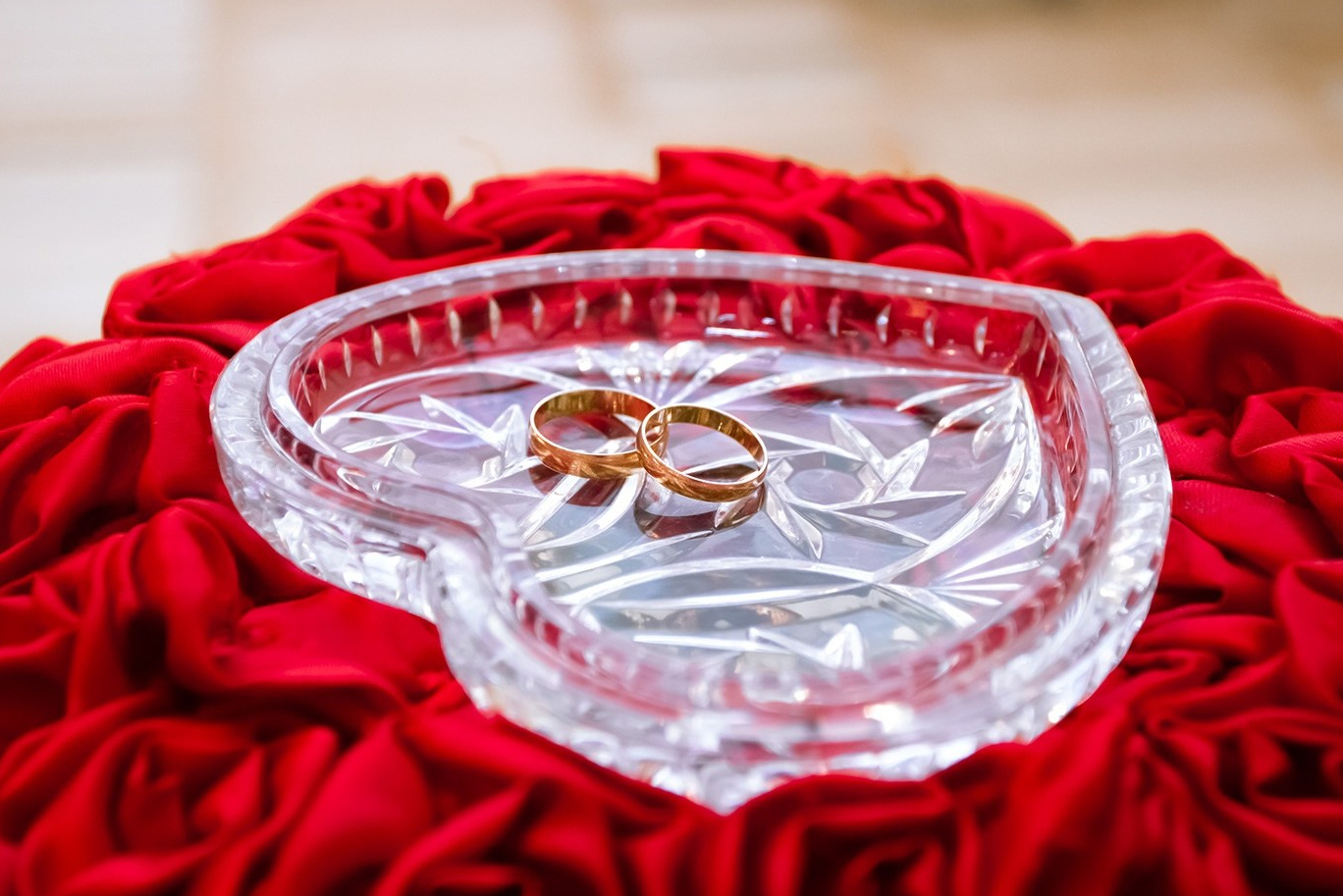 Свадебные кольца расположены в стеклянном блюдечке в форме сердца