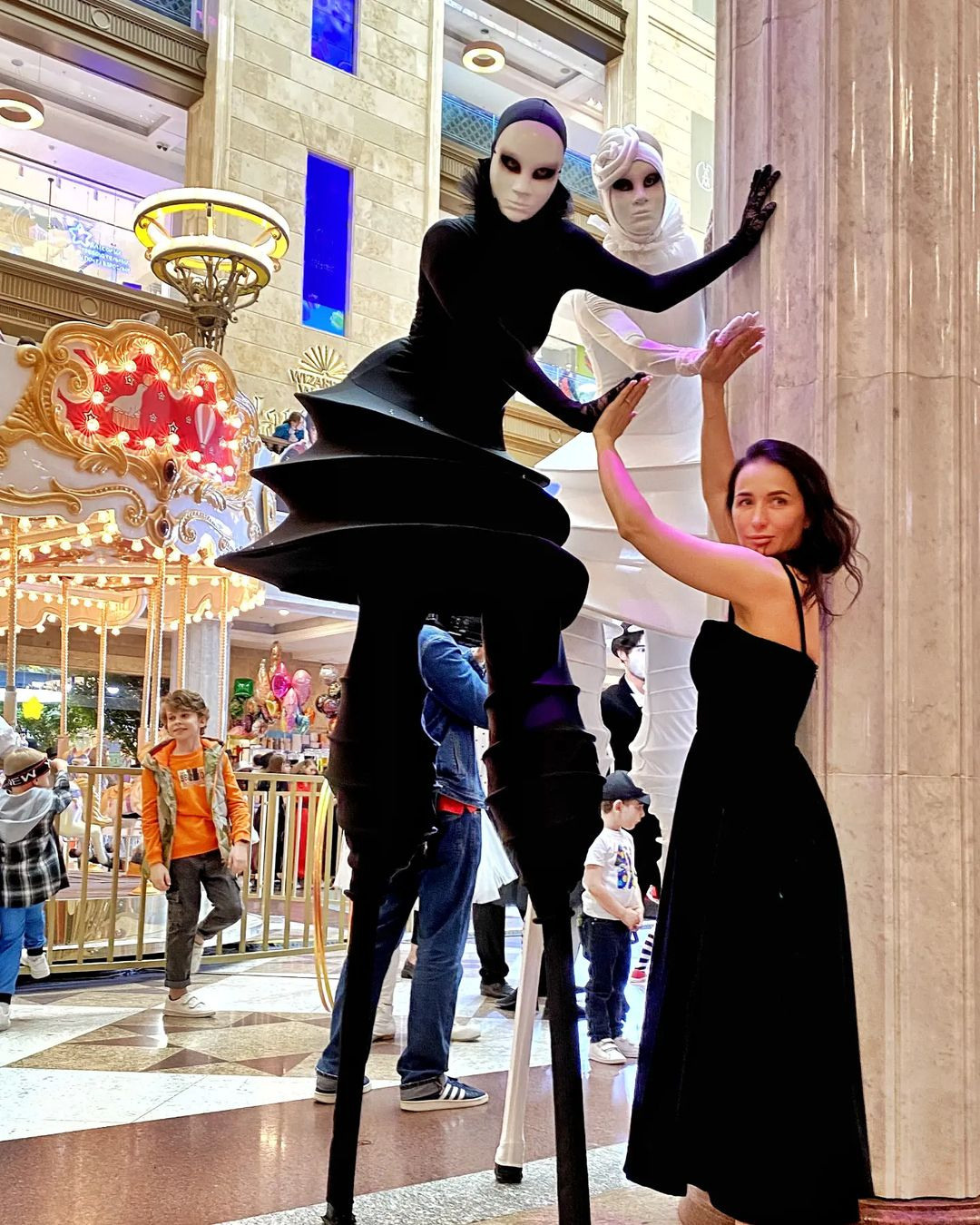 Ходулист в чёрном протягивает руку гостю и оба позируют фотографу.