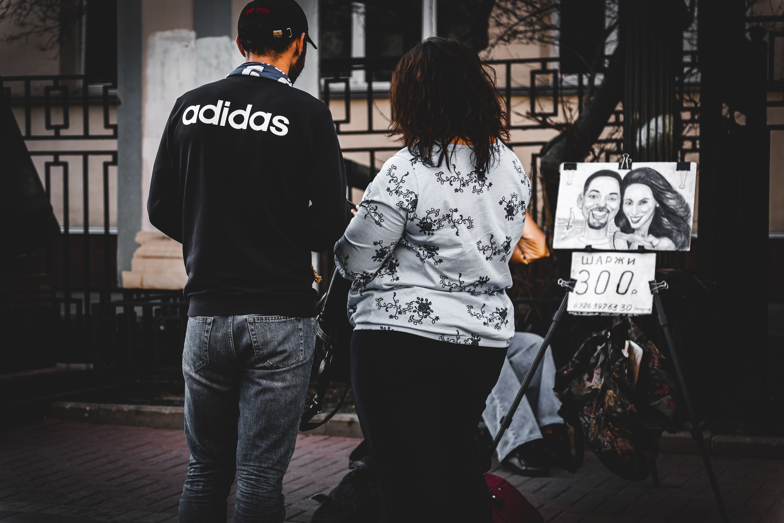 Двое людей рассматривают шаржи на Старом Арбате в Москве