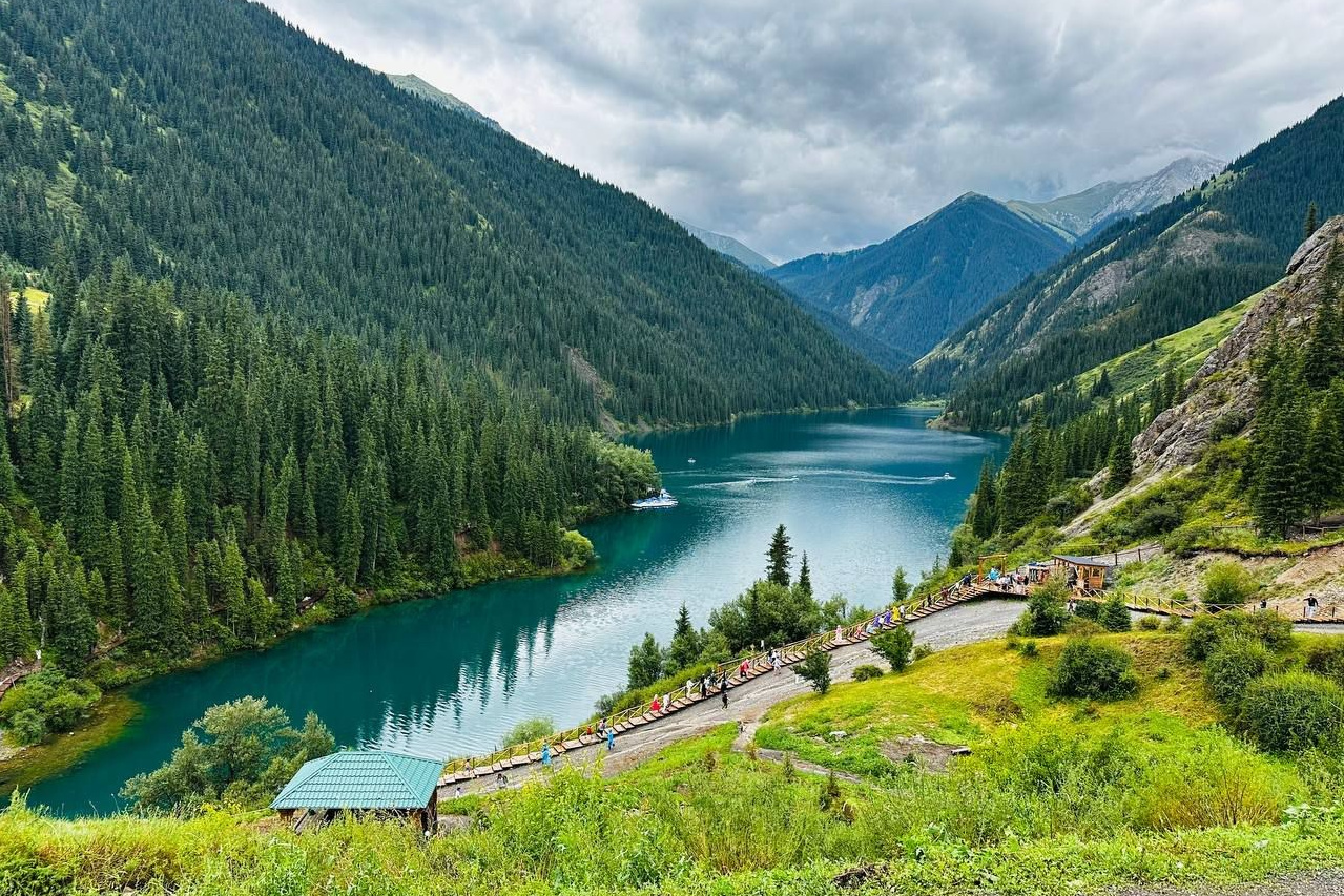 Вид на озеро Кольсай, окруженное хвойными лесами и горами, с туристической зоной и деревянной тропой на переднем плане, Алматы, Казахстан