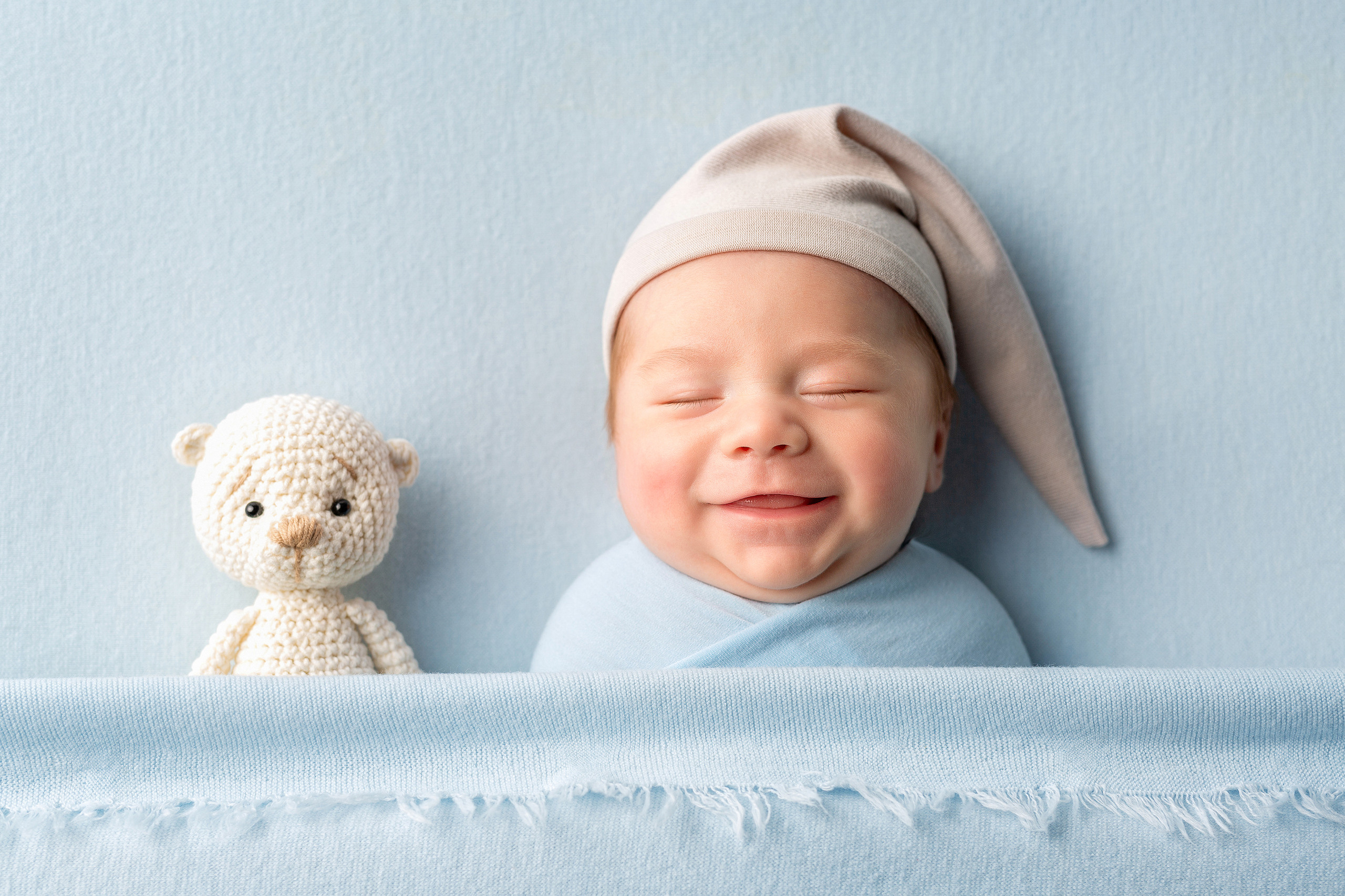 Новорожденный малыш улыбается, рядом маленькая игрушка мишка.