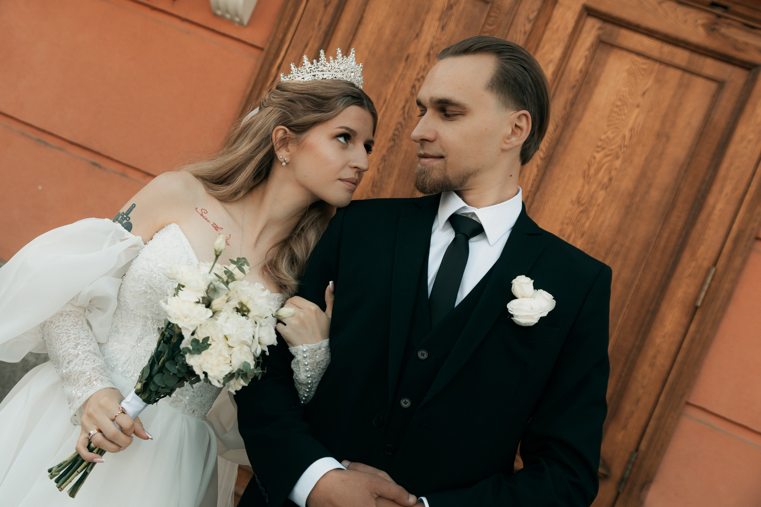 Молодожёны обнимаются на улице, невеста держит букет.