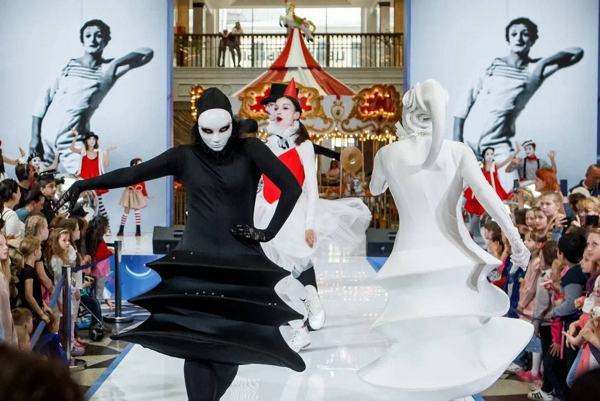 Белый и чёрный ходулисты идут на камеру по подиуму в Центральном Детском мире.