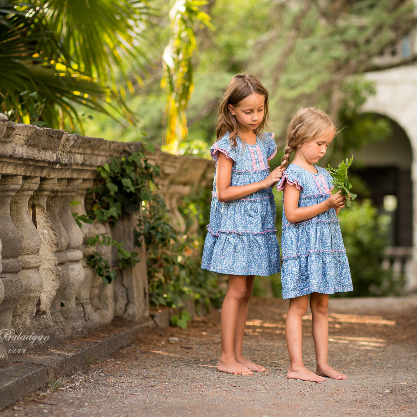 Две маленькие девочки сестры в одинаковых платьях плетут косы