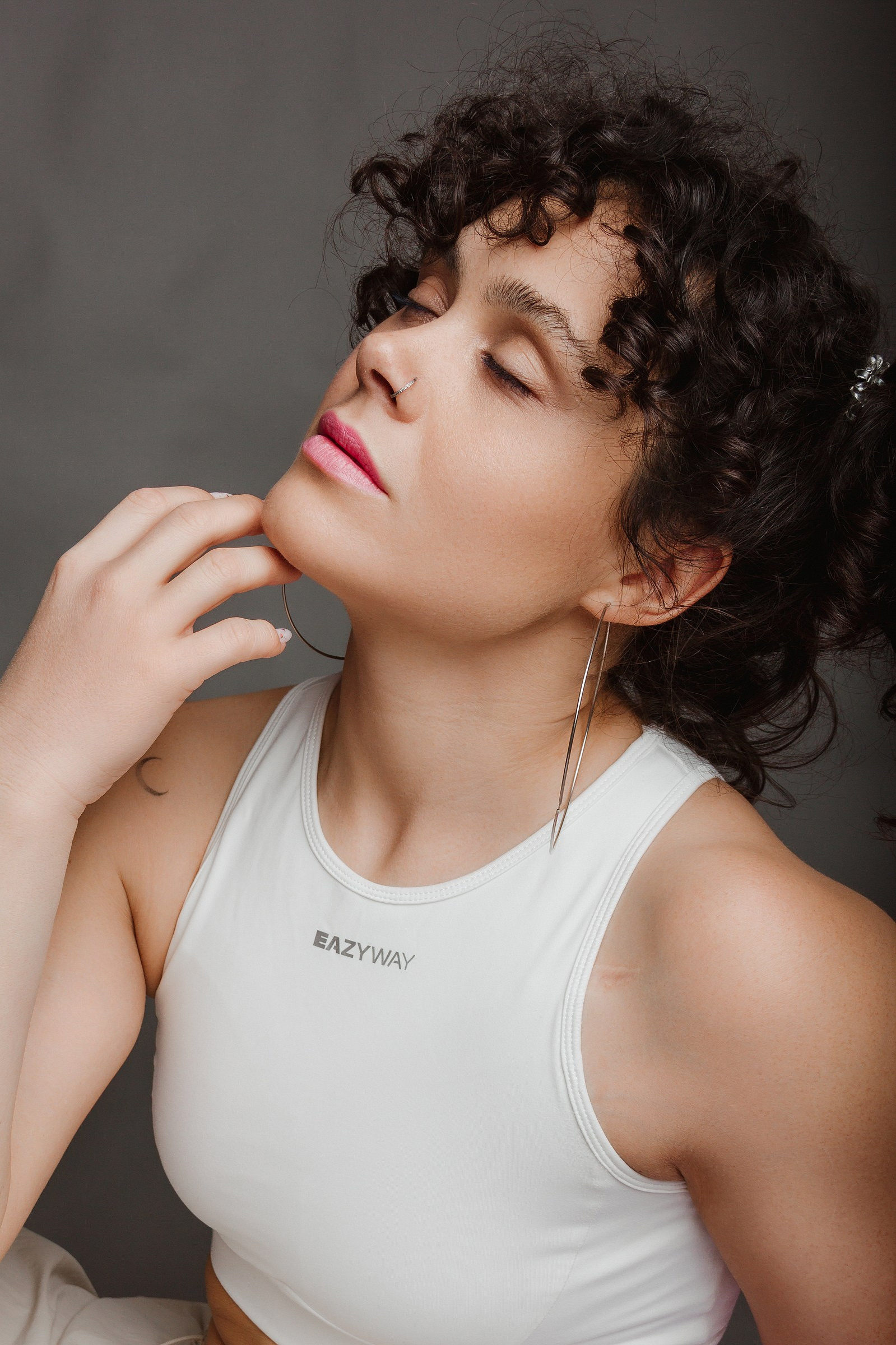 Темноволосая кудрявая девушка с закрытыми глазами на сером фоне