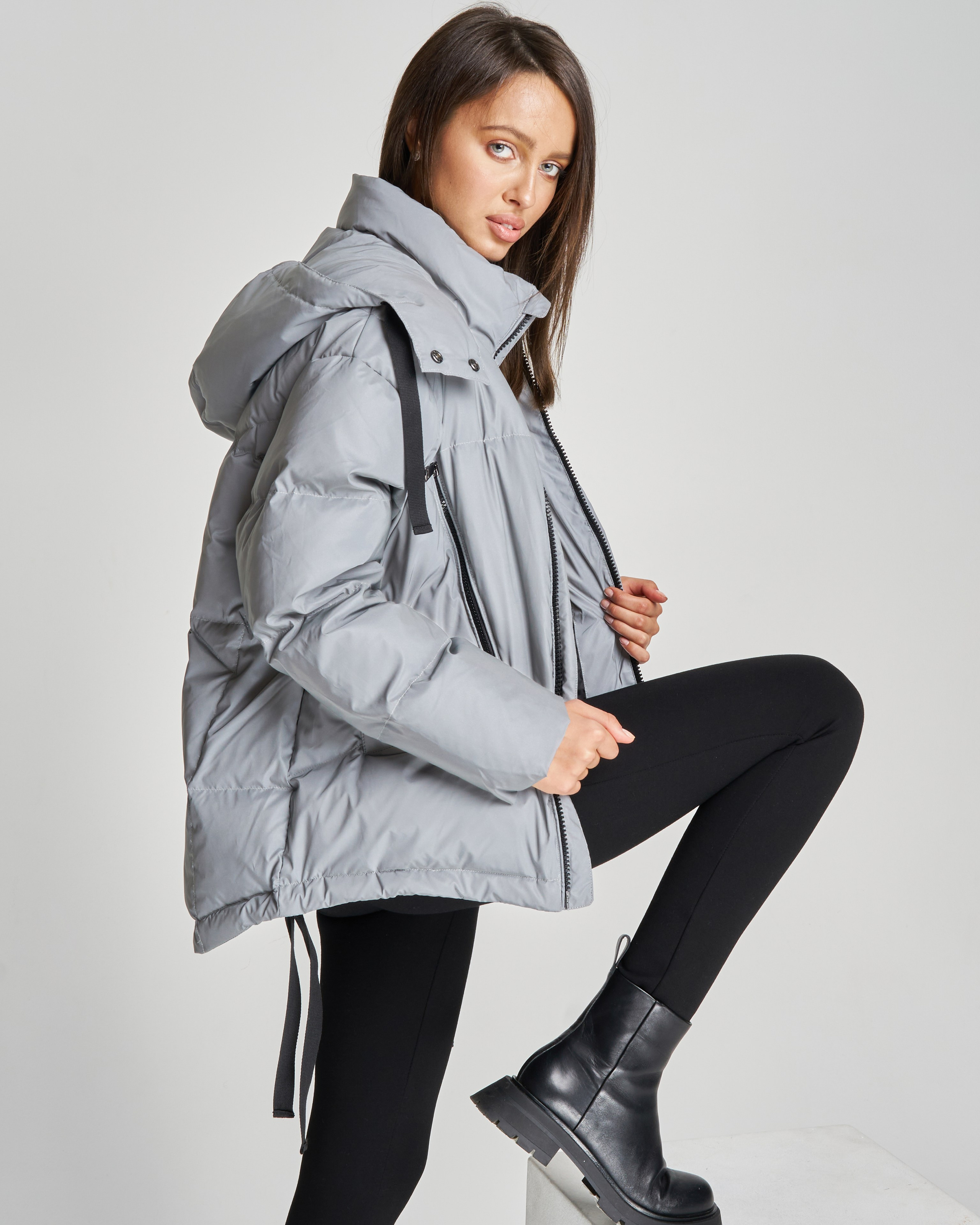 Девушка модель в серой куртке поставила ногу на подставку