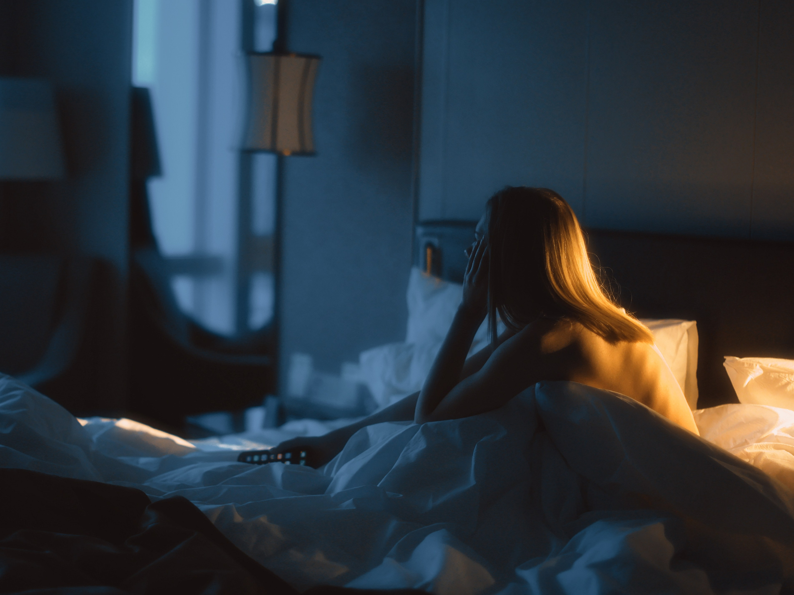 Девушка с голой спиной сидит в одиночестве в номере отеля.