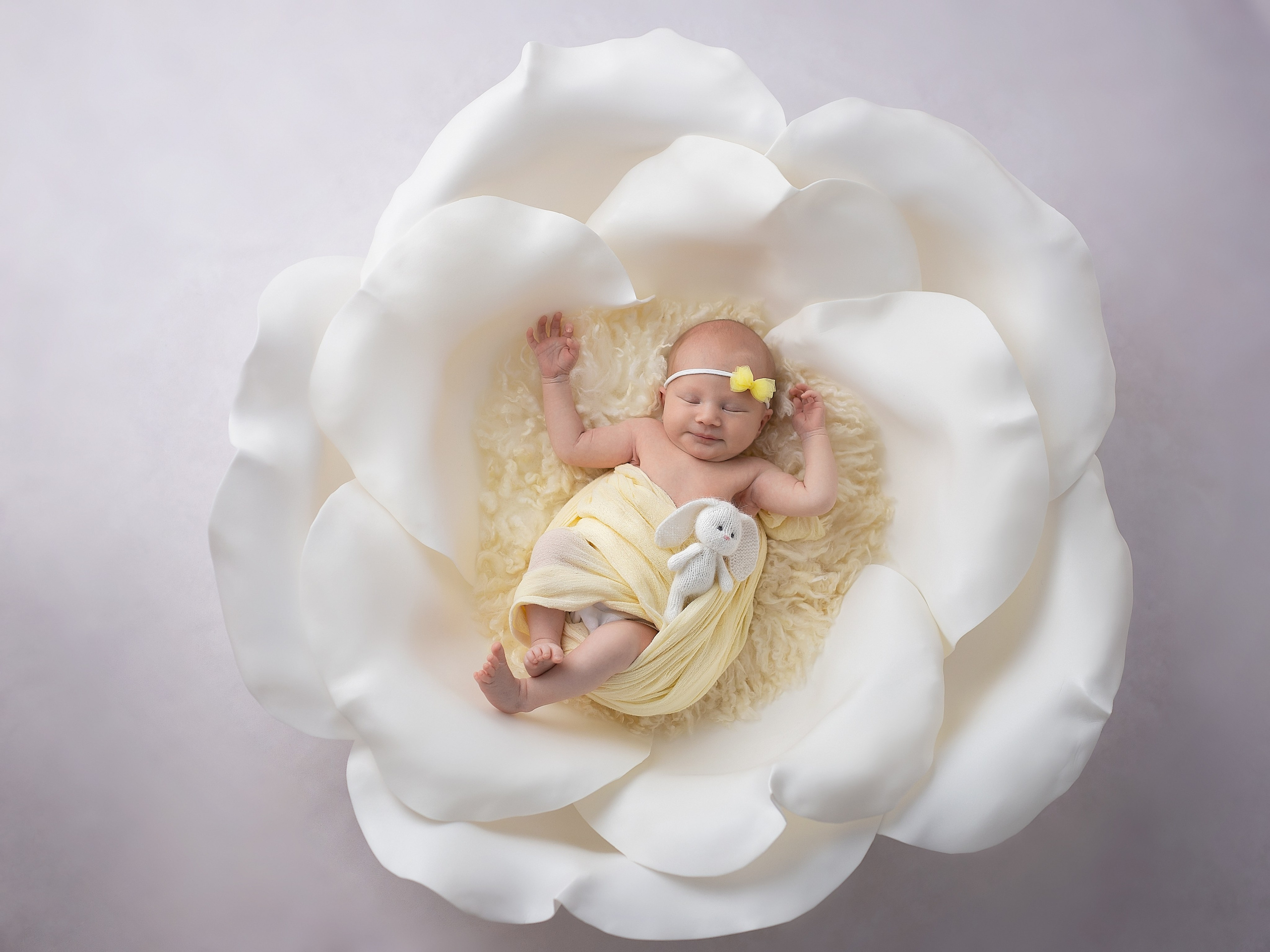 Маленькая девочка с желтым бантиком на голове лежит в большом цветке 