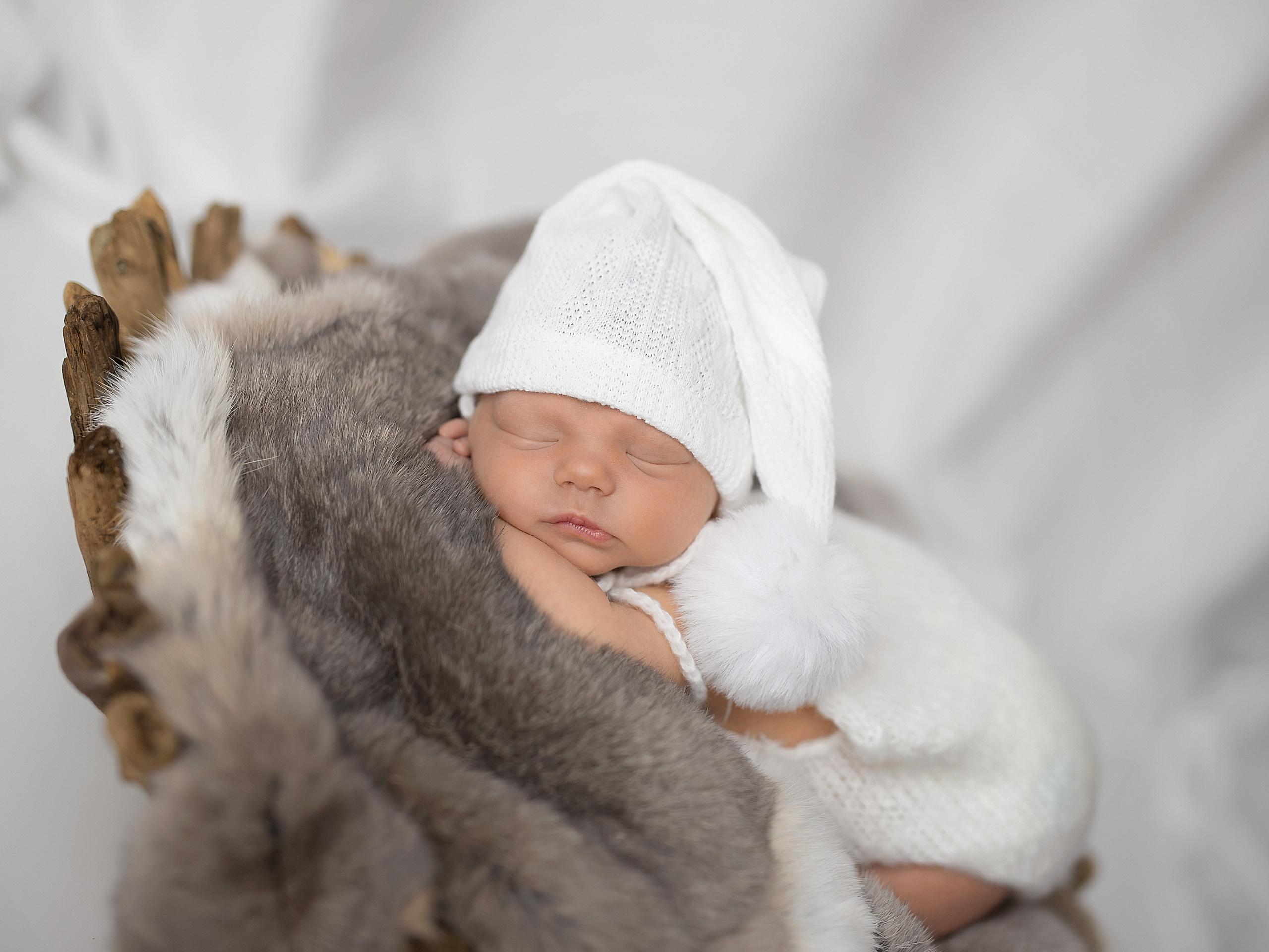 Новорожденный в белом колпаке спит на животике на мехе