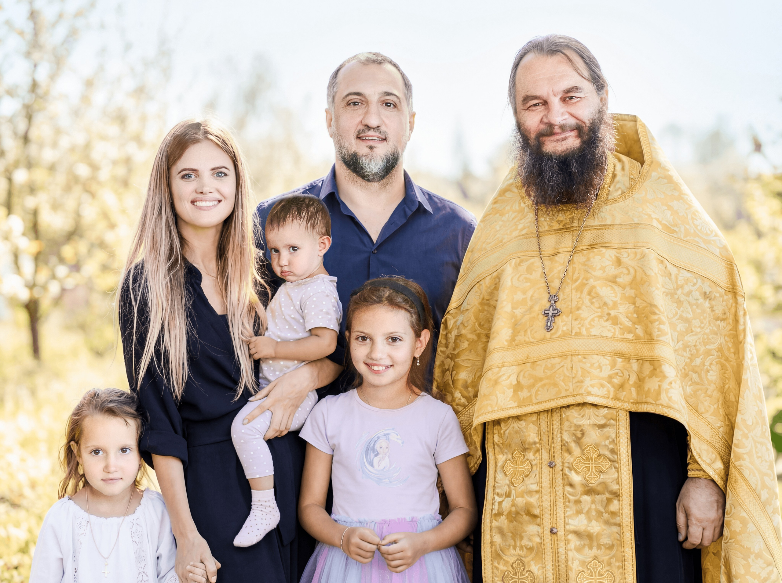 Родители с детьми и батюшкой улыбаются после крещения 