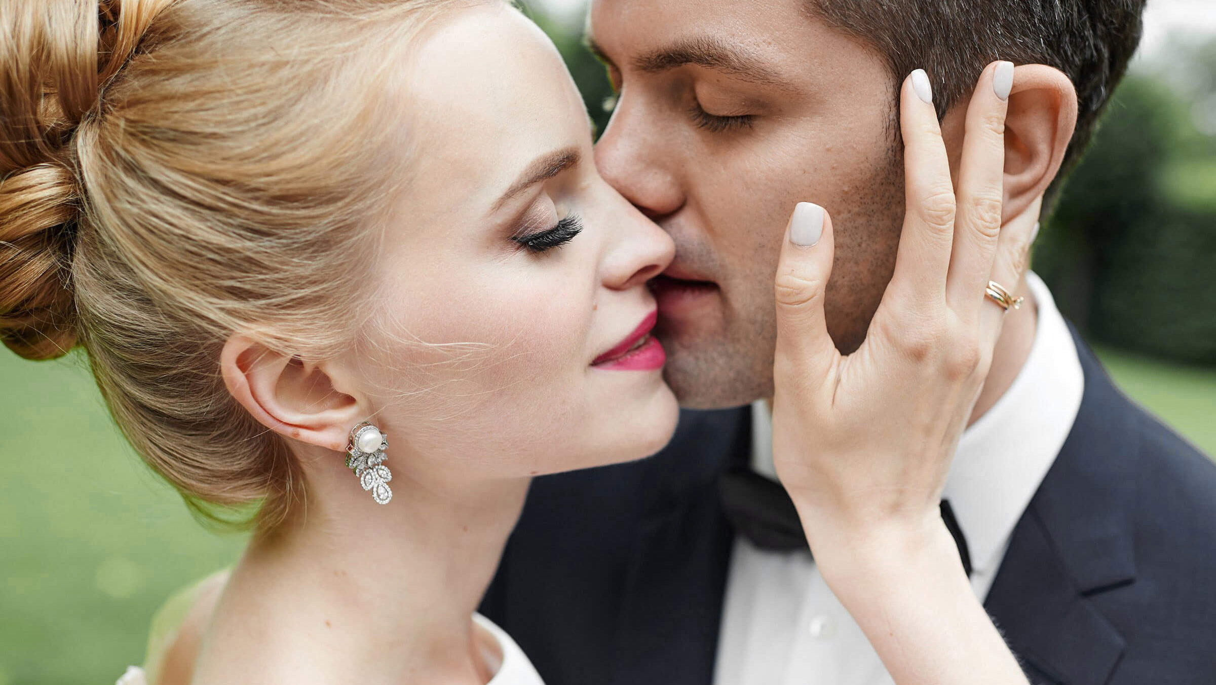 Эмоциональный момент: жених нежно целует невесту в щёку. Крупный план лиц, нежный кадр. Размытый фон подчёркивает интимность сцены. Естественное освещение, тёплые тона.