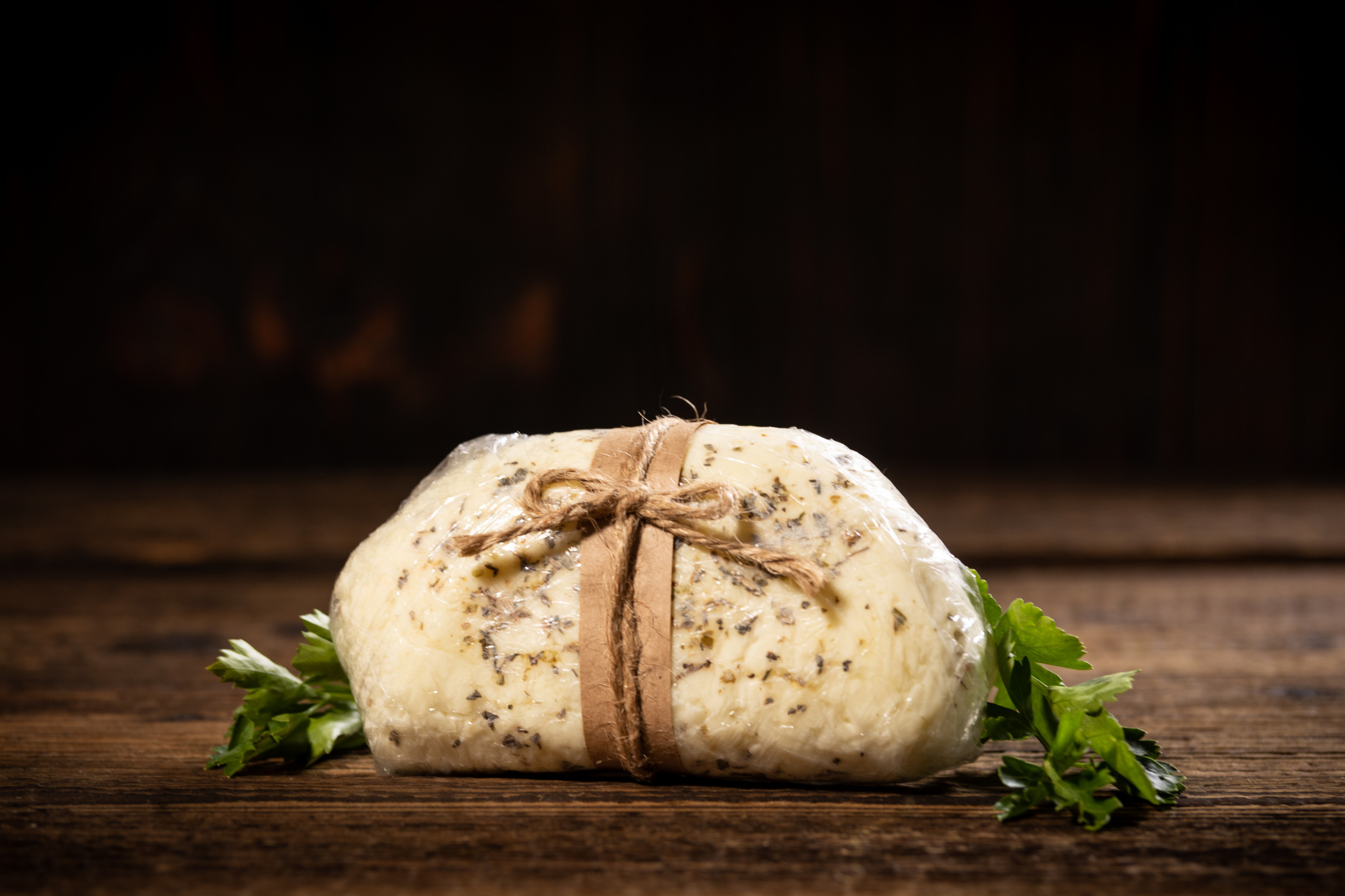 Головка сыра халлуми с прованскими травами, упакованная в пищевую пленку.