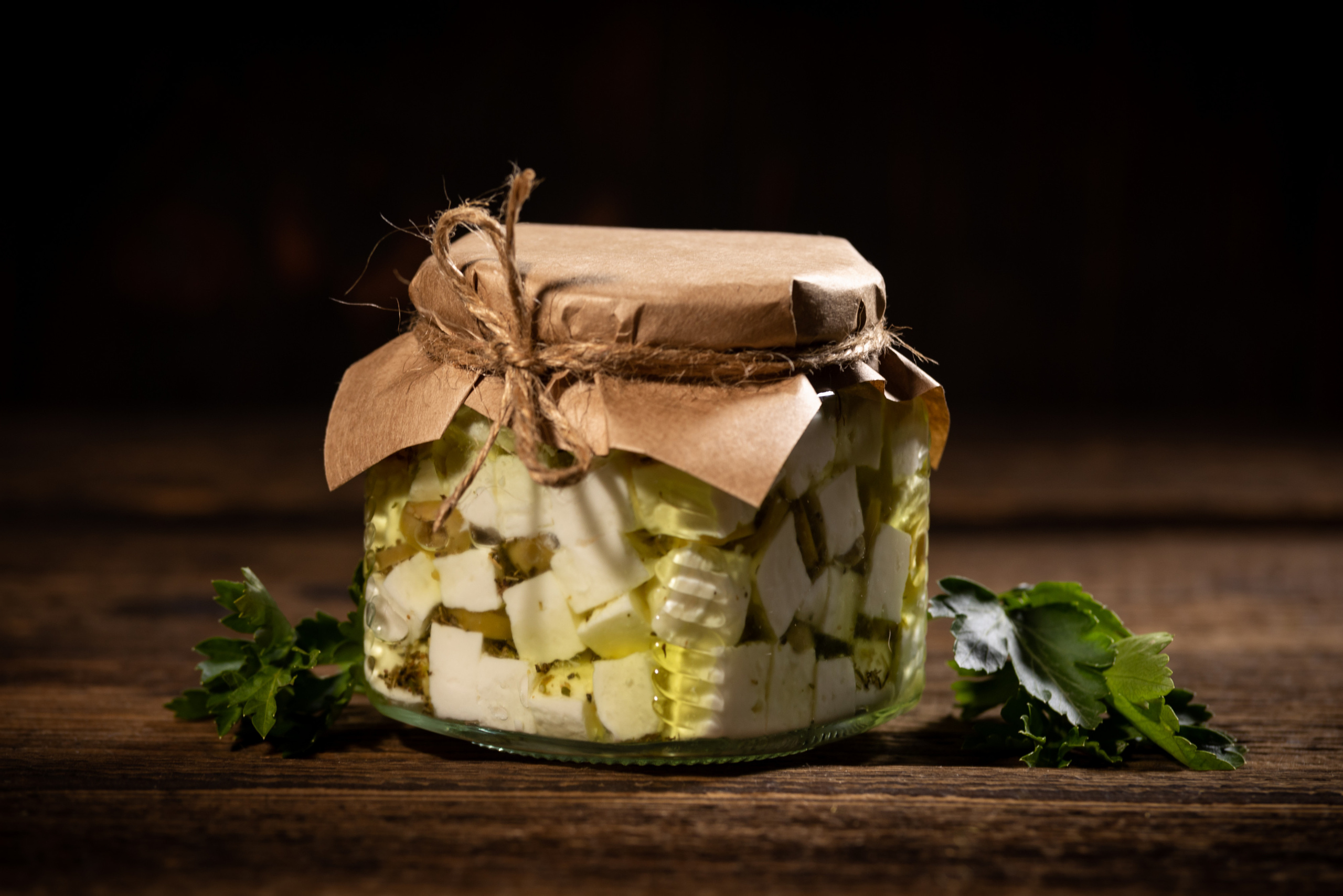 Стеклянная банка 250 мл с сыром фета в оливковом масле крупным планом на фоне состаренных досок