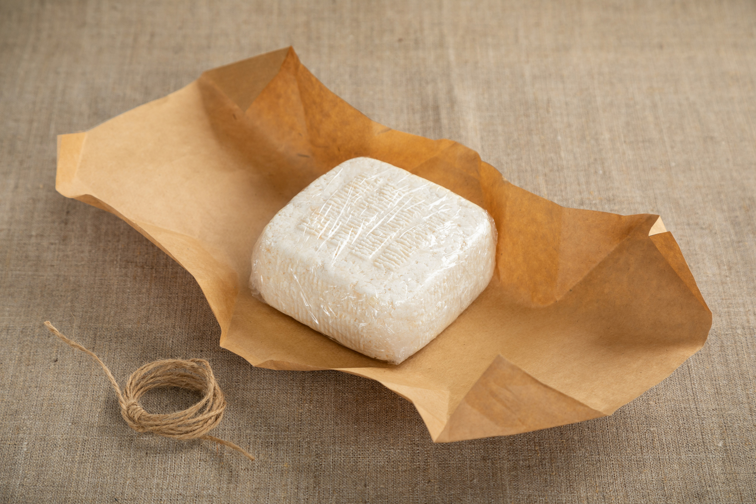 Головка классического адыгейского сыра развернутой упаковке из крафтовой бумаги.