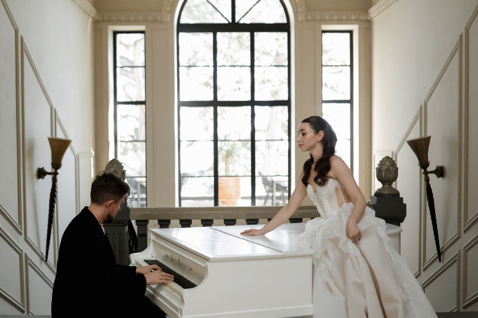 Жених играет на рояле, рядом невеста в свадебном платье  
