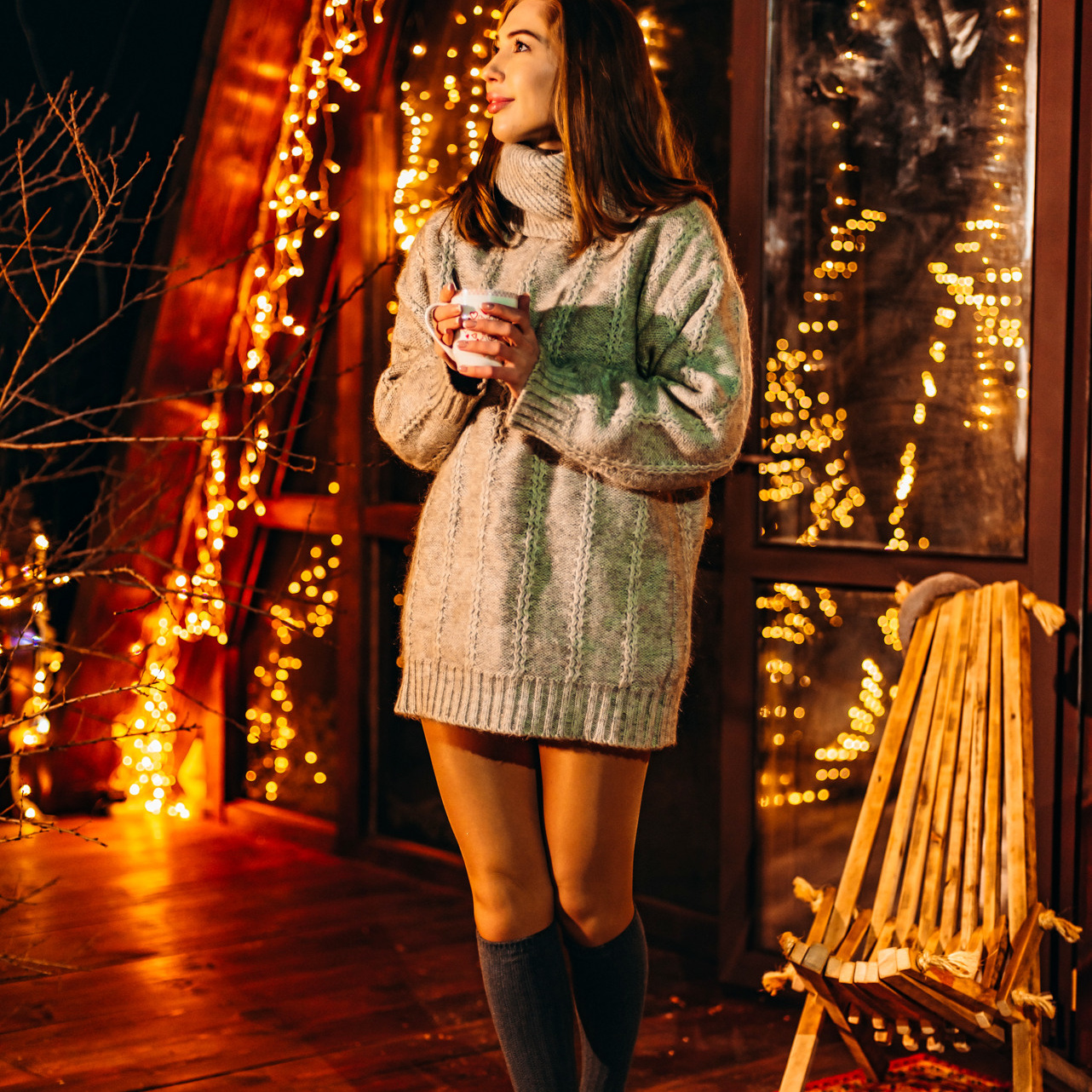 Семейная фотосессия в Иркутске Девушка в сером свитере и гетрах на веранде треугольного дома с гирляндами